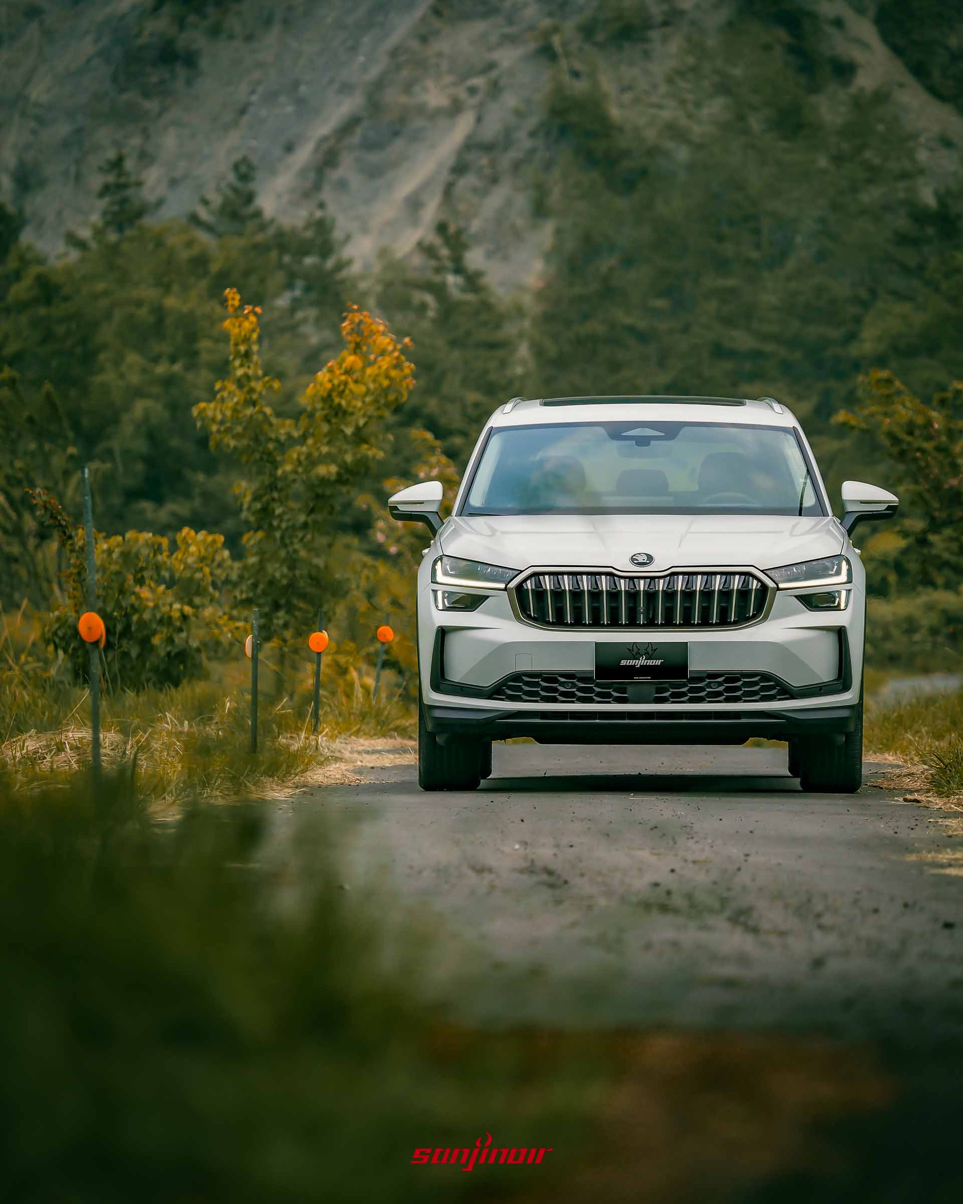 白色 Škoda Kodiaq 2.0 TSI 4×4 行駛在路上的正面特寫照片，路旁有橘色反光標誌，背景是山脈與樹林。