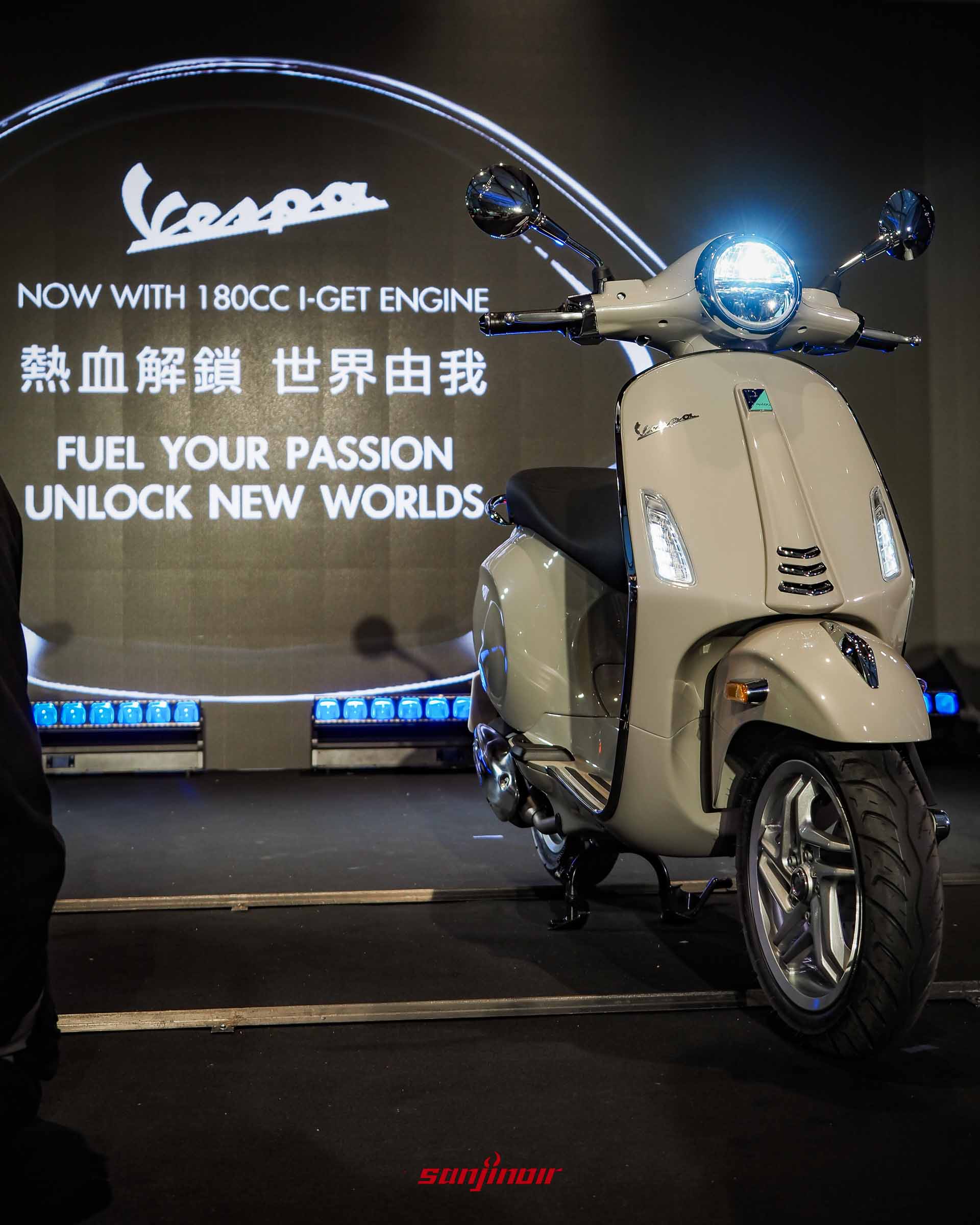 發表會舞台上展示的白色Vespa Primavera180斜前方視角,車身鍍鉻件在燈光下閃爍。