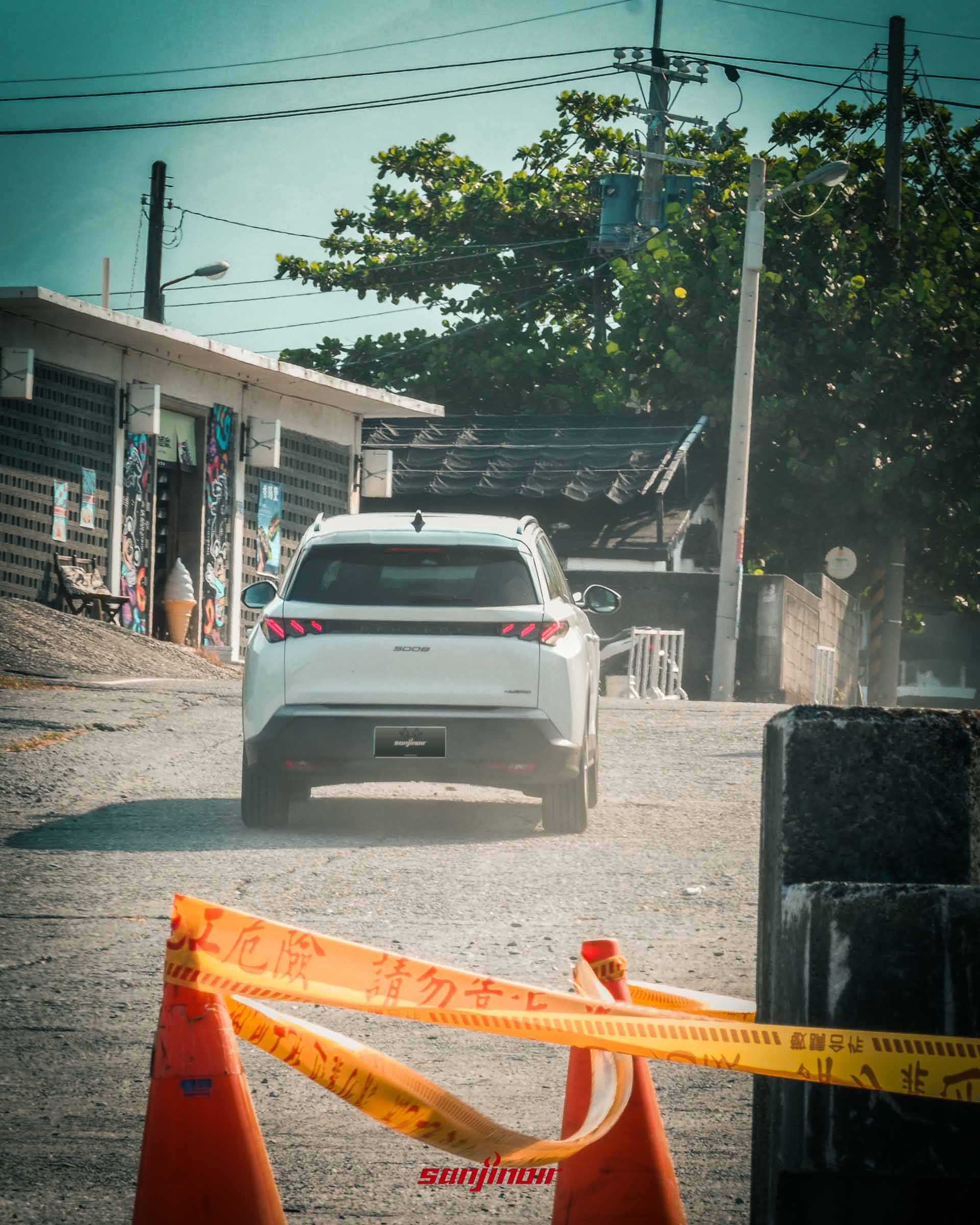 白色PEUGEOT 5008行駛於上坡小路的車尾照,前景有模糊的橘色三角錐與黃色施工警告封鎖線。