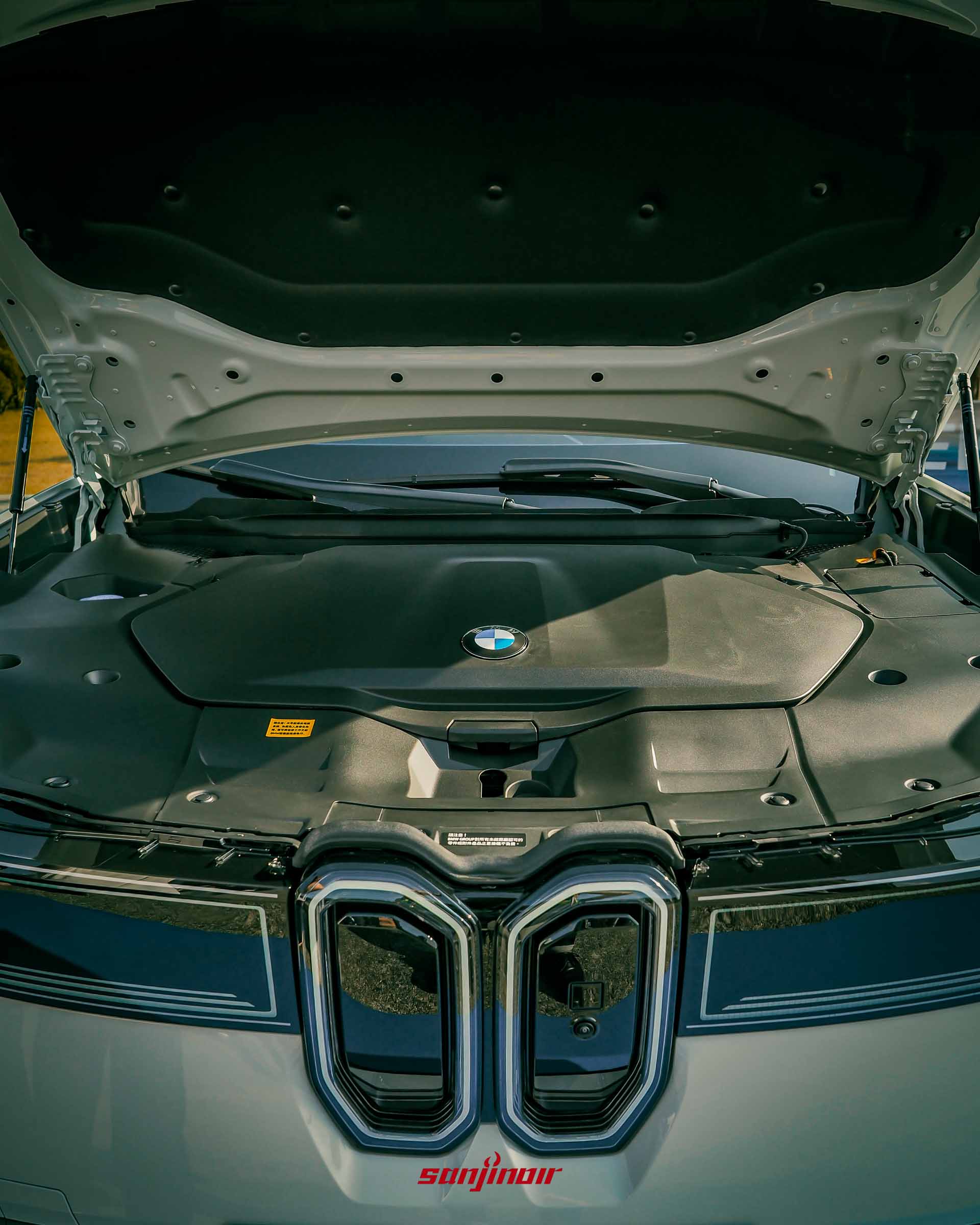 BMW iX3車頭引擎蓋開啟特寫，內部護蓋平整，中央帶有BMW藍白廠徽，下方為雙腎型水箱護罩。