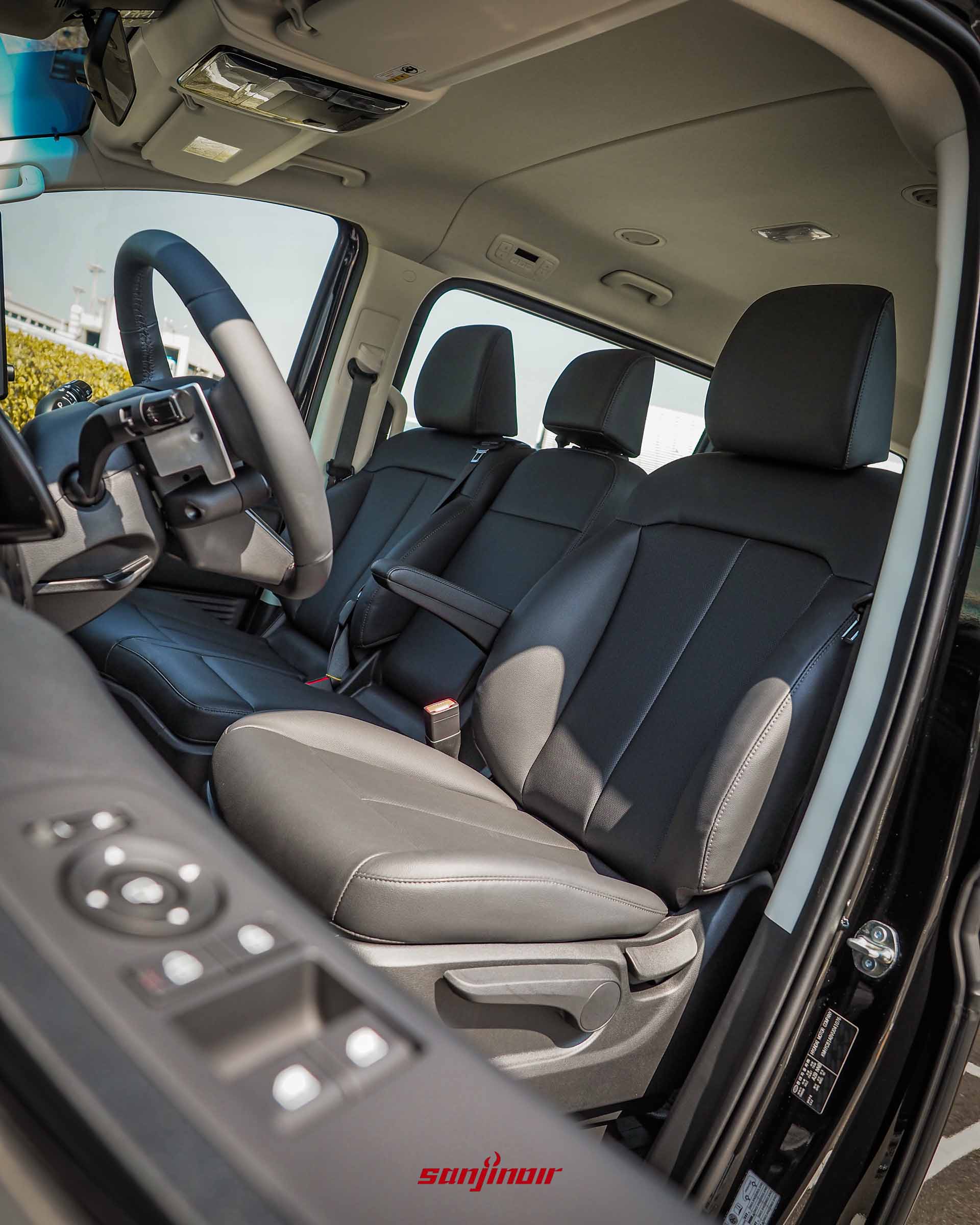 從副駕駛座側門向內拍攝 Hyundai Staria 前排座椅,展示其三人座配置與黑色皮質包覆設計。