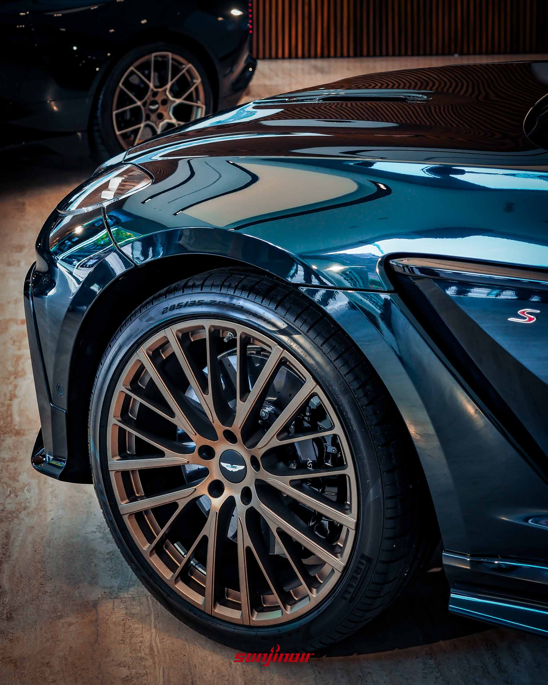 Aston Martin DBX S車側前輪局部特寫，展示深綠色車身烤漆、23吋古銅金多幅式輪圈、巨大的黑色煞車卡鉗與車側散熱孔旁的S字樣銘牌。