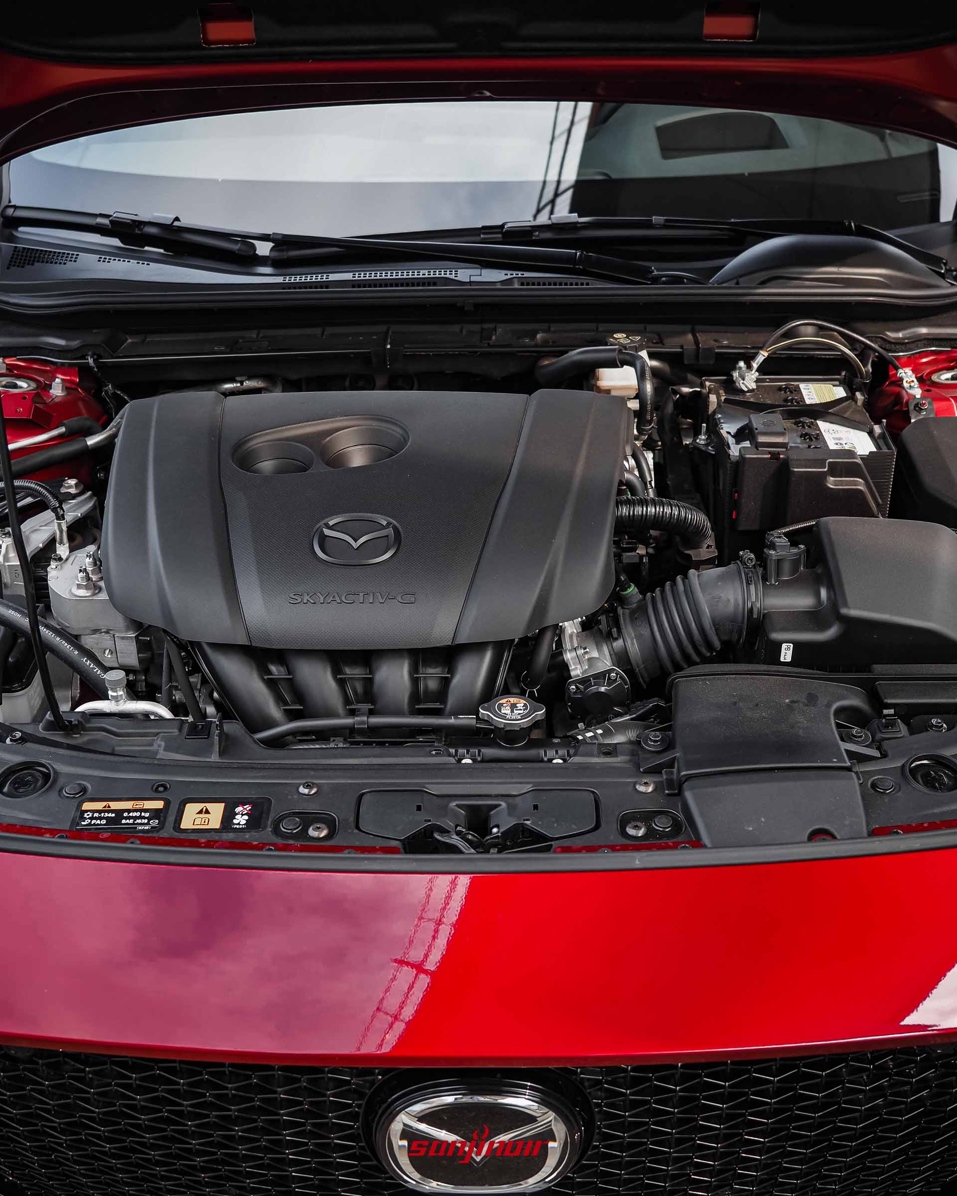 打開引擎蓋的MAZDA3 HOMURA，展示2.0L Skyactiv-G自然進氣引擎室配置，帶有MAZDA標誌的黑色引擎飾蓋清晰可見。