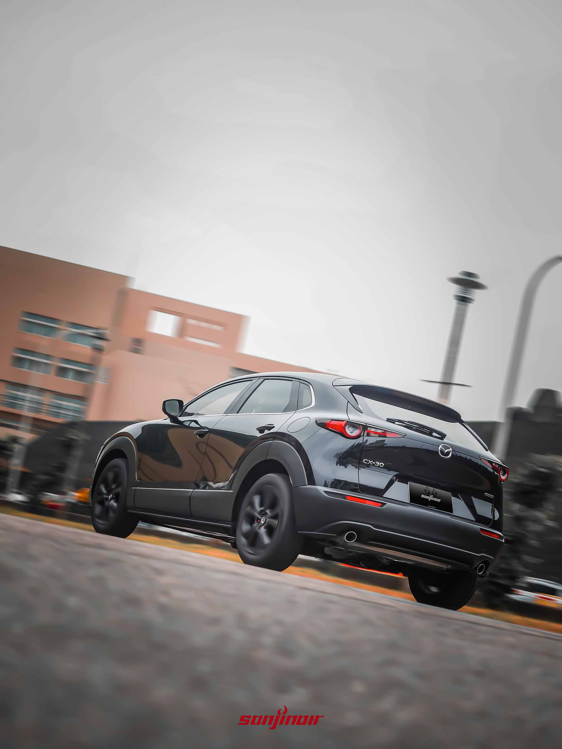 黑色MAZDA CX-30 20S Homura於道路上行駛的動態追焦照,展示其車尾流線動態。