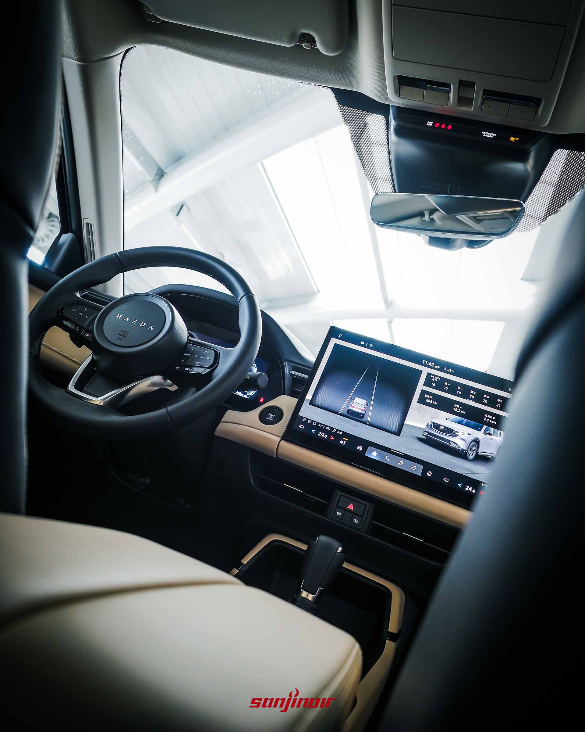 從副駕駛座後方視角拍攝MAZDA CX-5前座駕駛艙,包含方向盤與中控大螢幕。