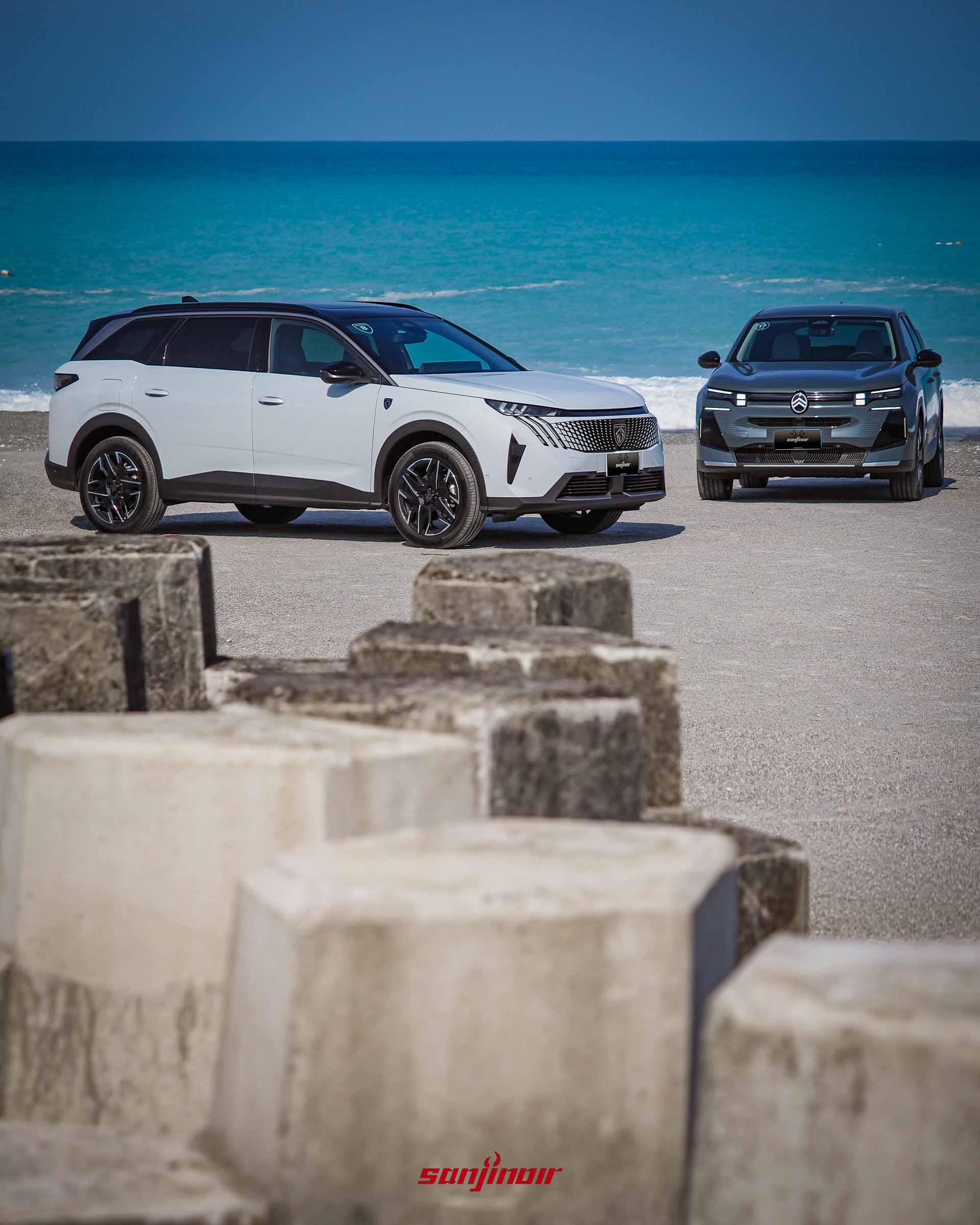 白色PEUGEOT 5008與綠色CITROËN C5 Aircross停放在海岸邊的合照,前景為水泥消波塊,背景為湛藍海洋與天空。