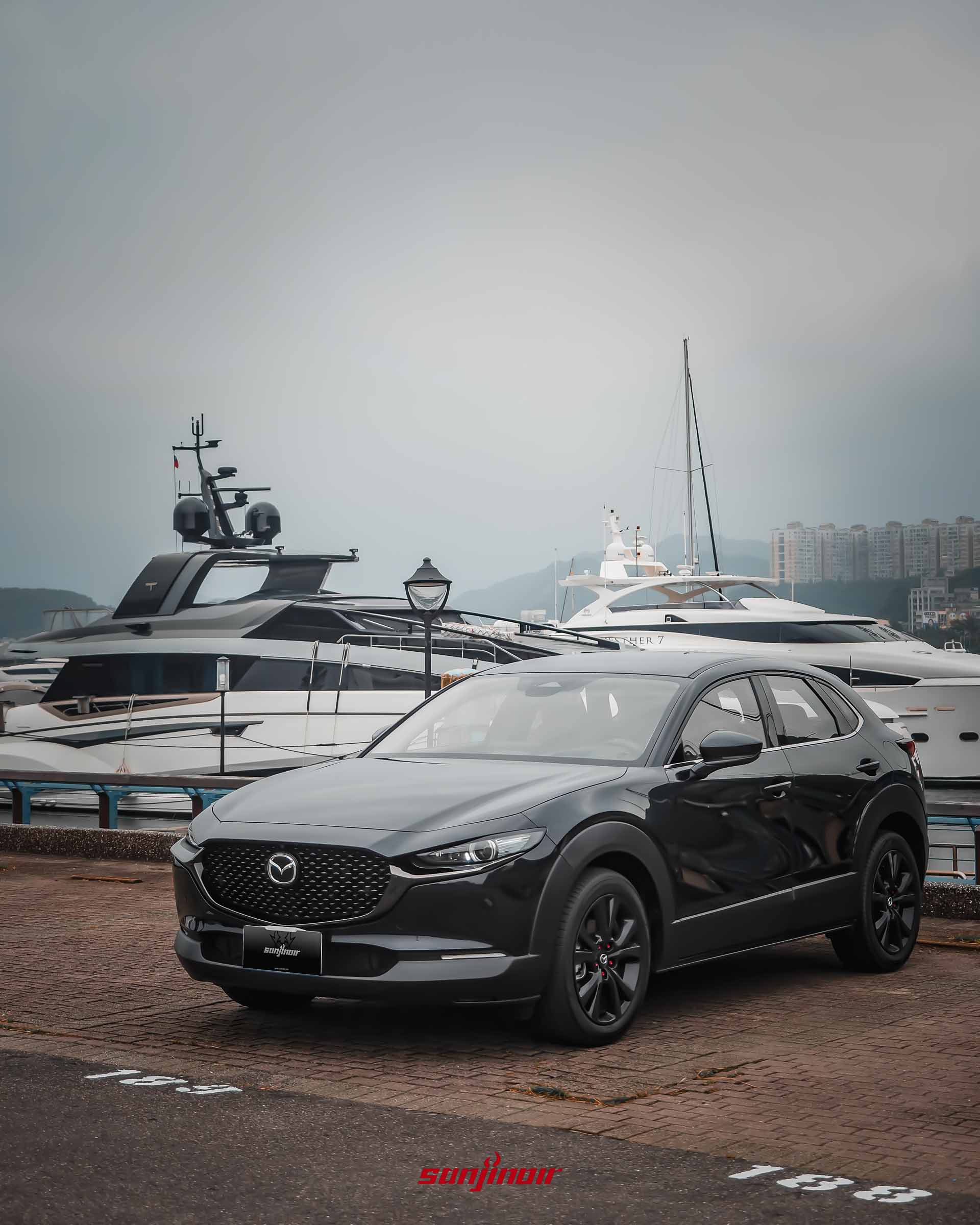 黑色MAZDA CX-30 20S Homura停放於碼頭,後方停泊著數艘大型豪華私人遊艇。