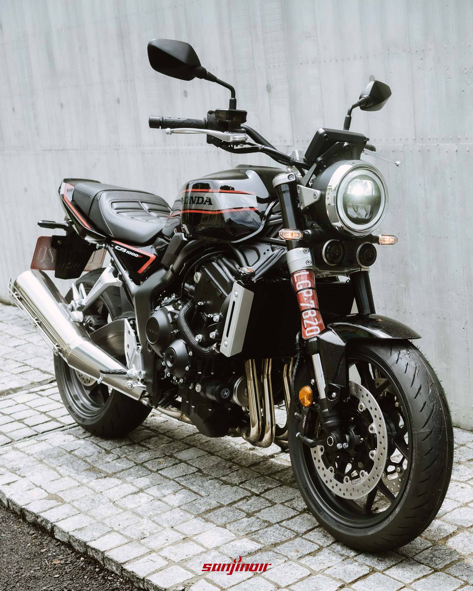 黑色Honda CB1000F點亮頭燈停放於石板路上的右前方45度角全車照片,背景為清水模。