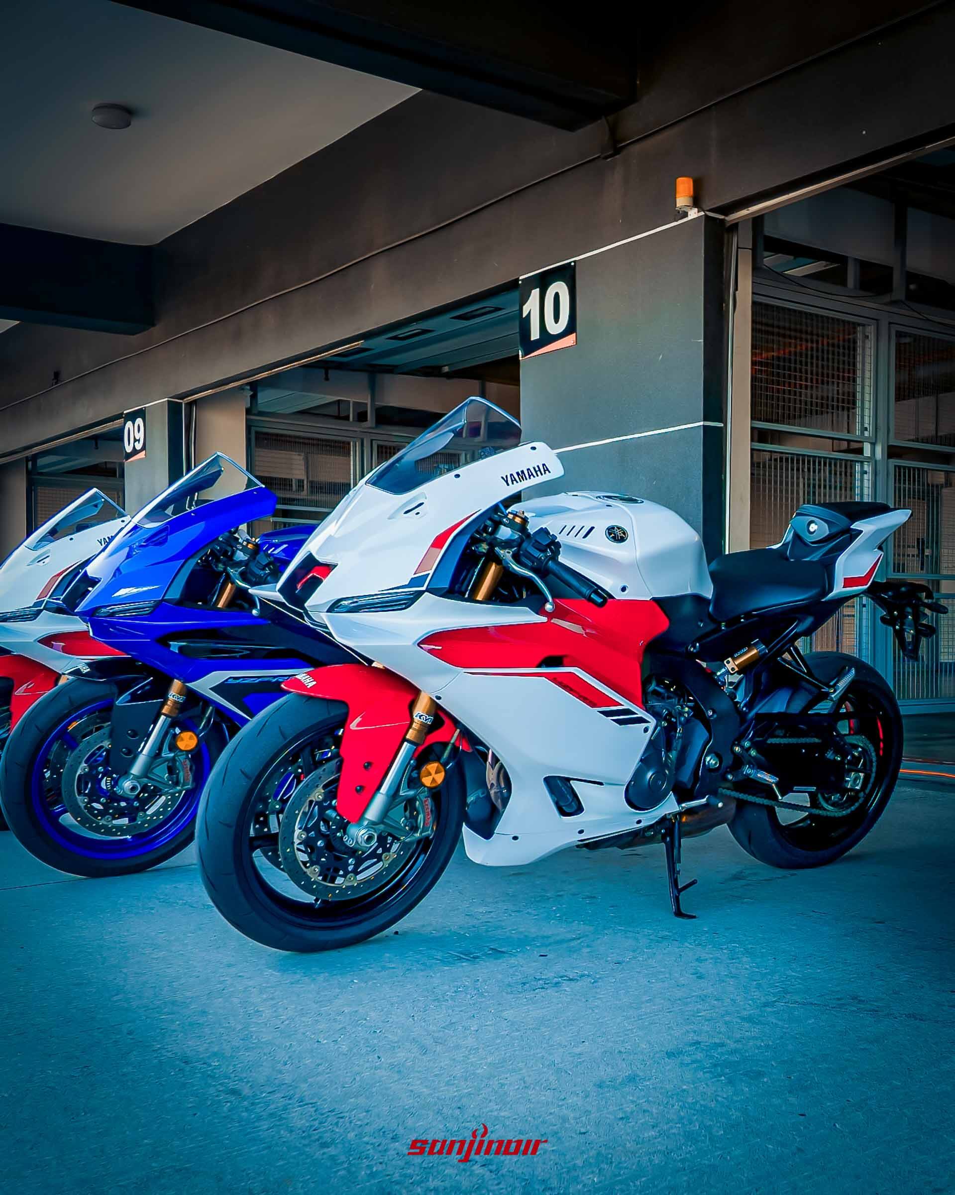 三輛Yamaha YZF-R9停放在賽車場的維修區車庫前,最前方為白紅配色的70週年紀念版,後方兩輛為競技藍配色。