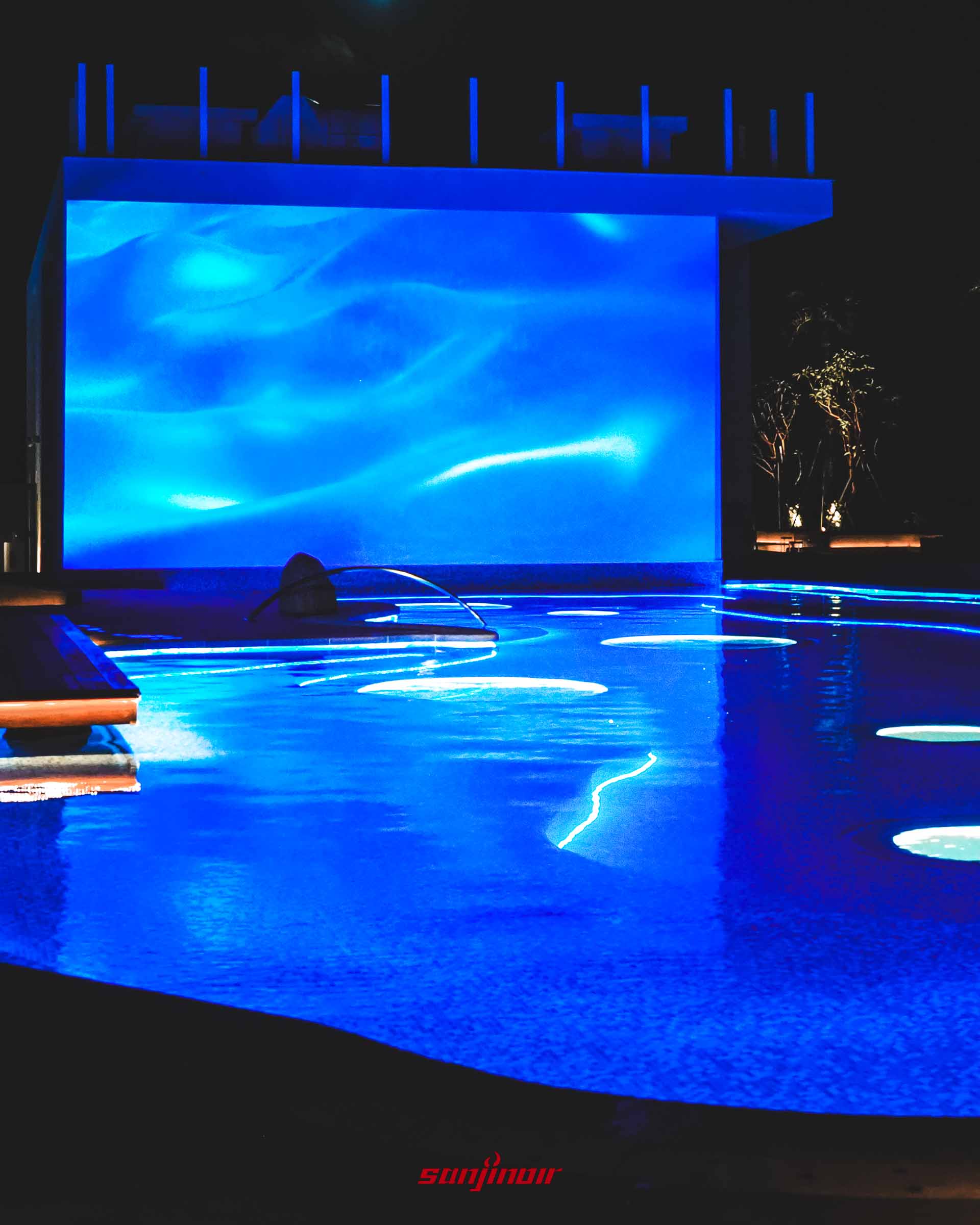 夜間的頂樓空中泳池,池水透出湛藍光芒,後方巨大的螢幕正播放著藍色波浪動畫。
