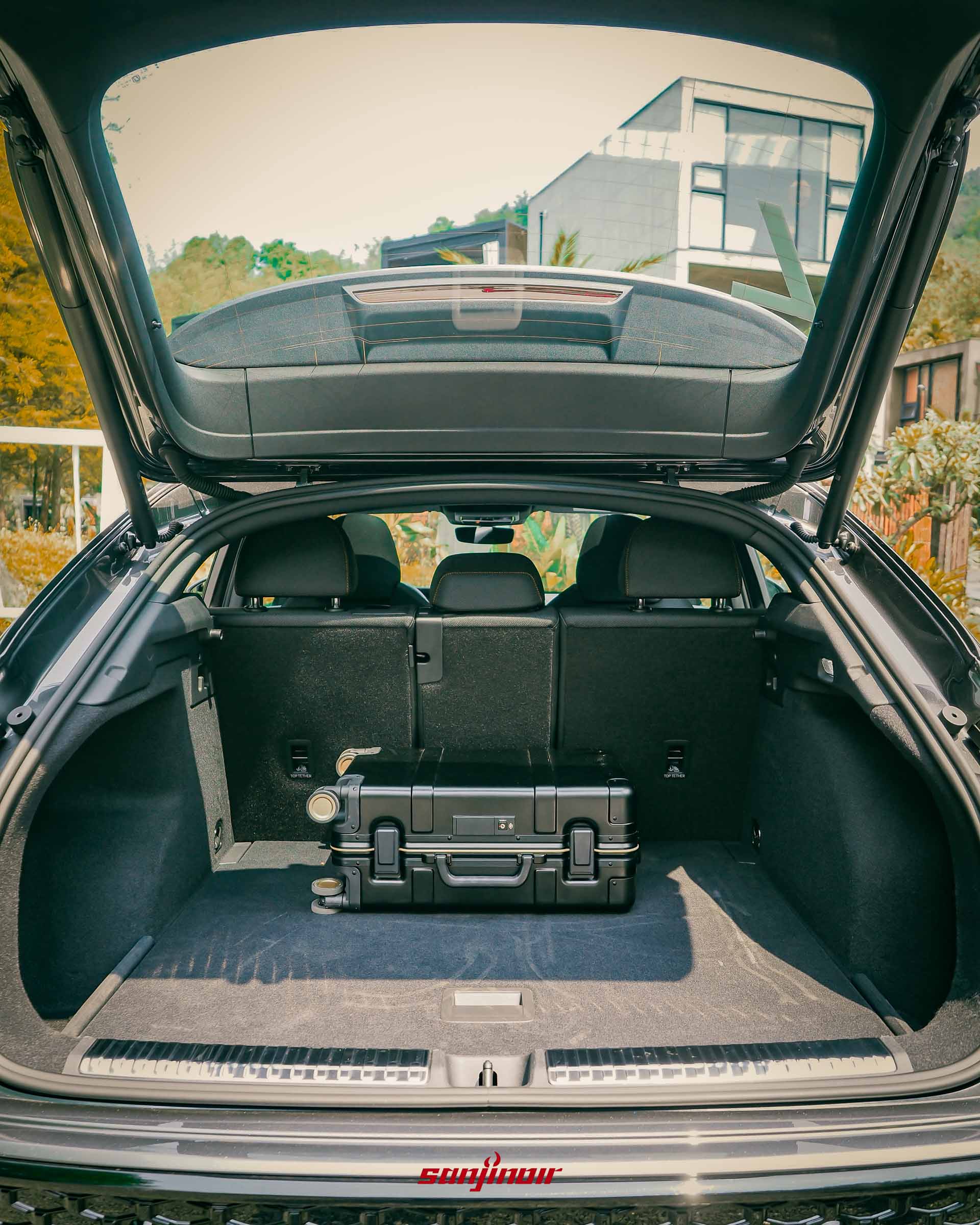 Audi Q3後車廂開啟，內部放置了一個黑色的硬殼行李箱，展示空間深度。