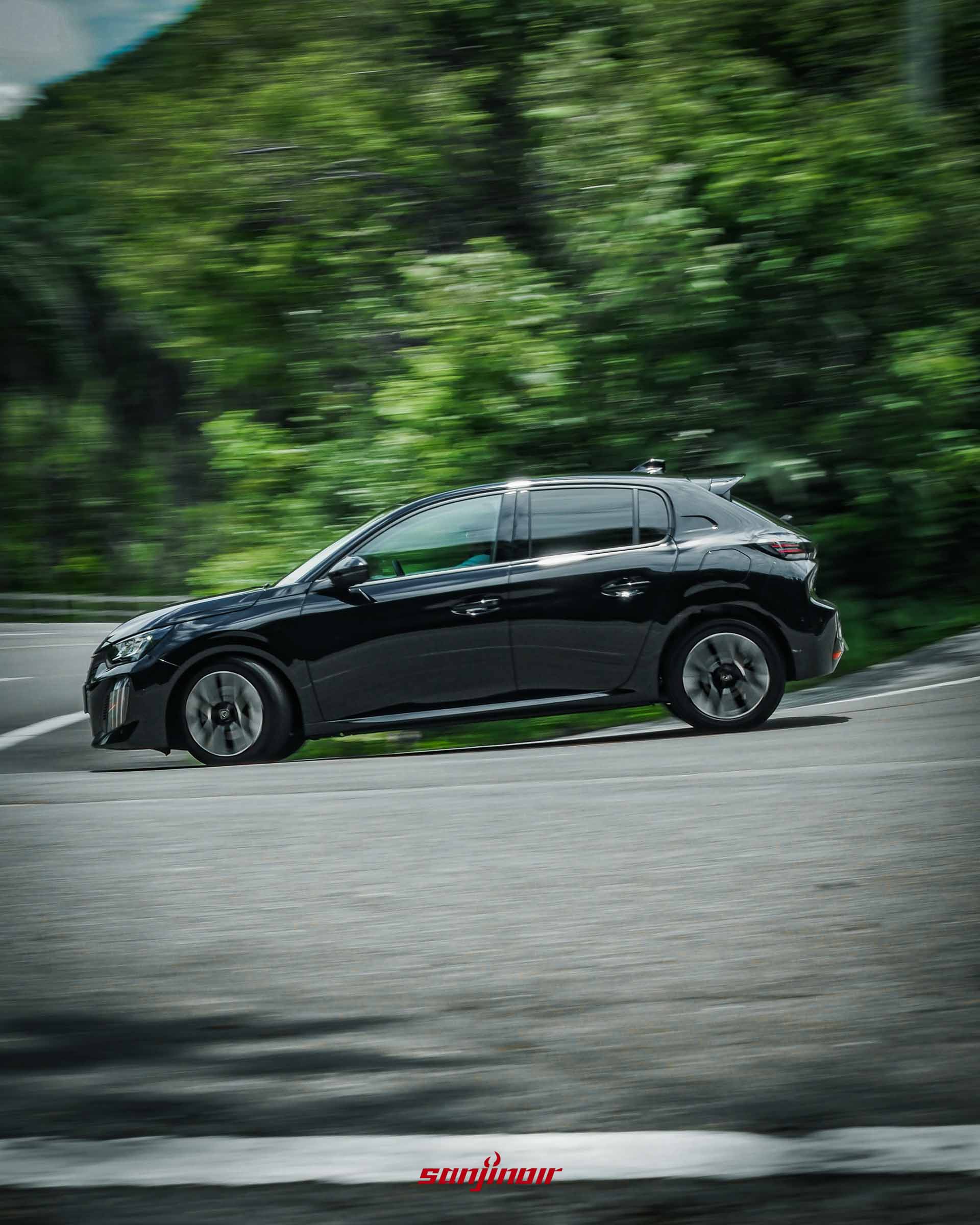 黑色PEUGEOT 208 Hybrid行駛於山林道路的側面動態追焦照。