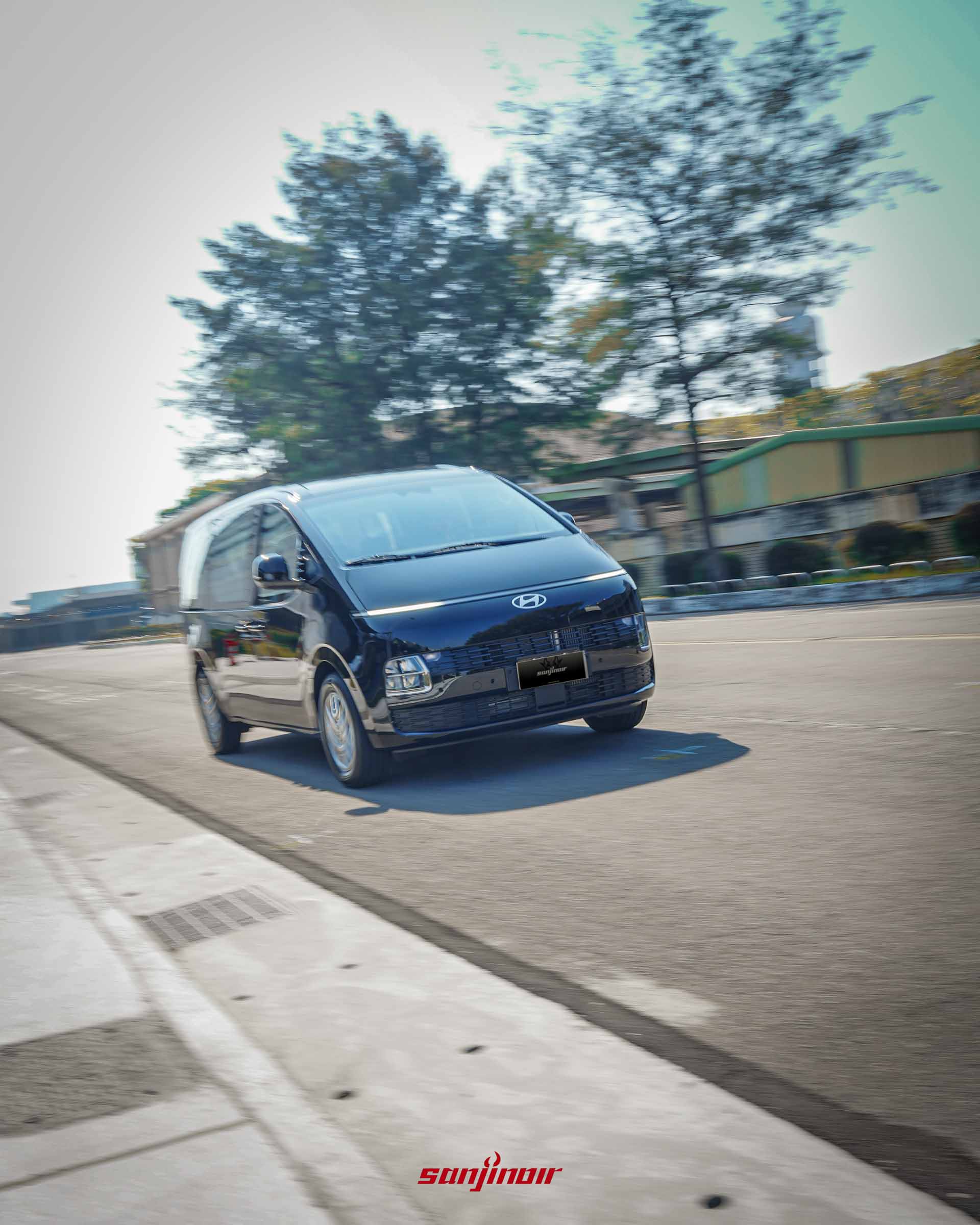 黑色 Hyundai Staria 在道路上行駛的動態追焦攝影,從右前側視角展現其破風前行的動感姿態。