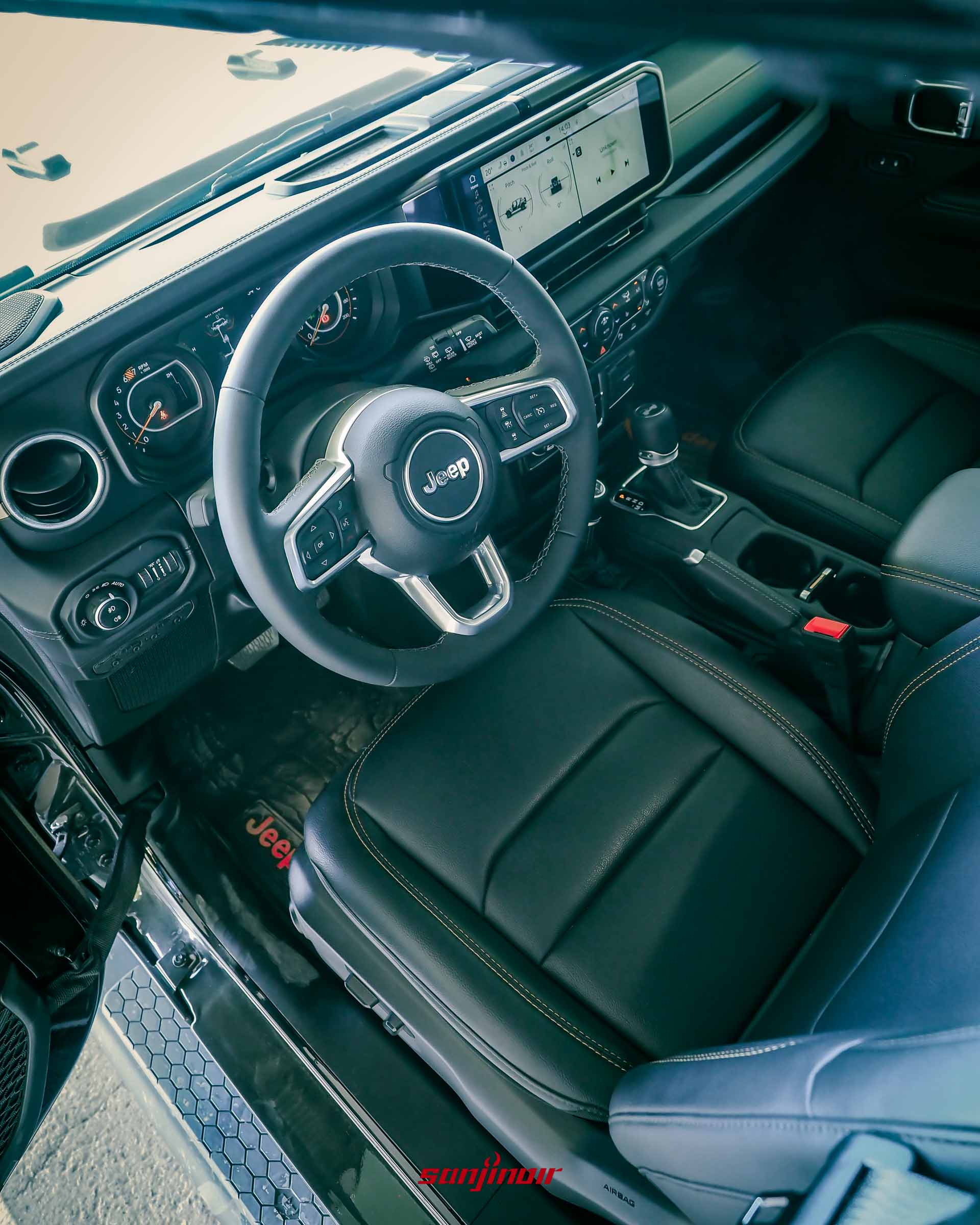 Jeep Wrangler Sahara 的駕駛座艙俯視角,可見皮質方向盤、數位儀錶板、中央觸控螢幕及實體按鍵區。