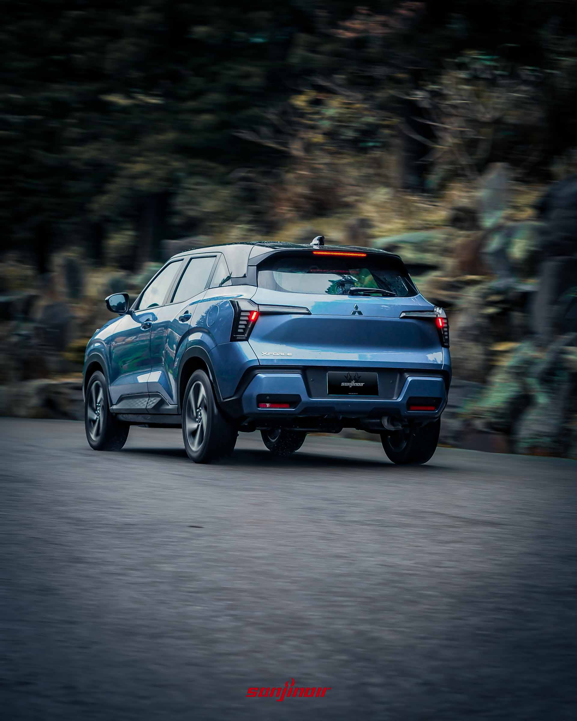 藍色Mitsubishi XForce狂享版在柏油山路上動態行駛的車尾視角。