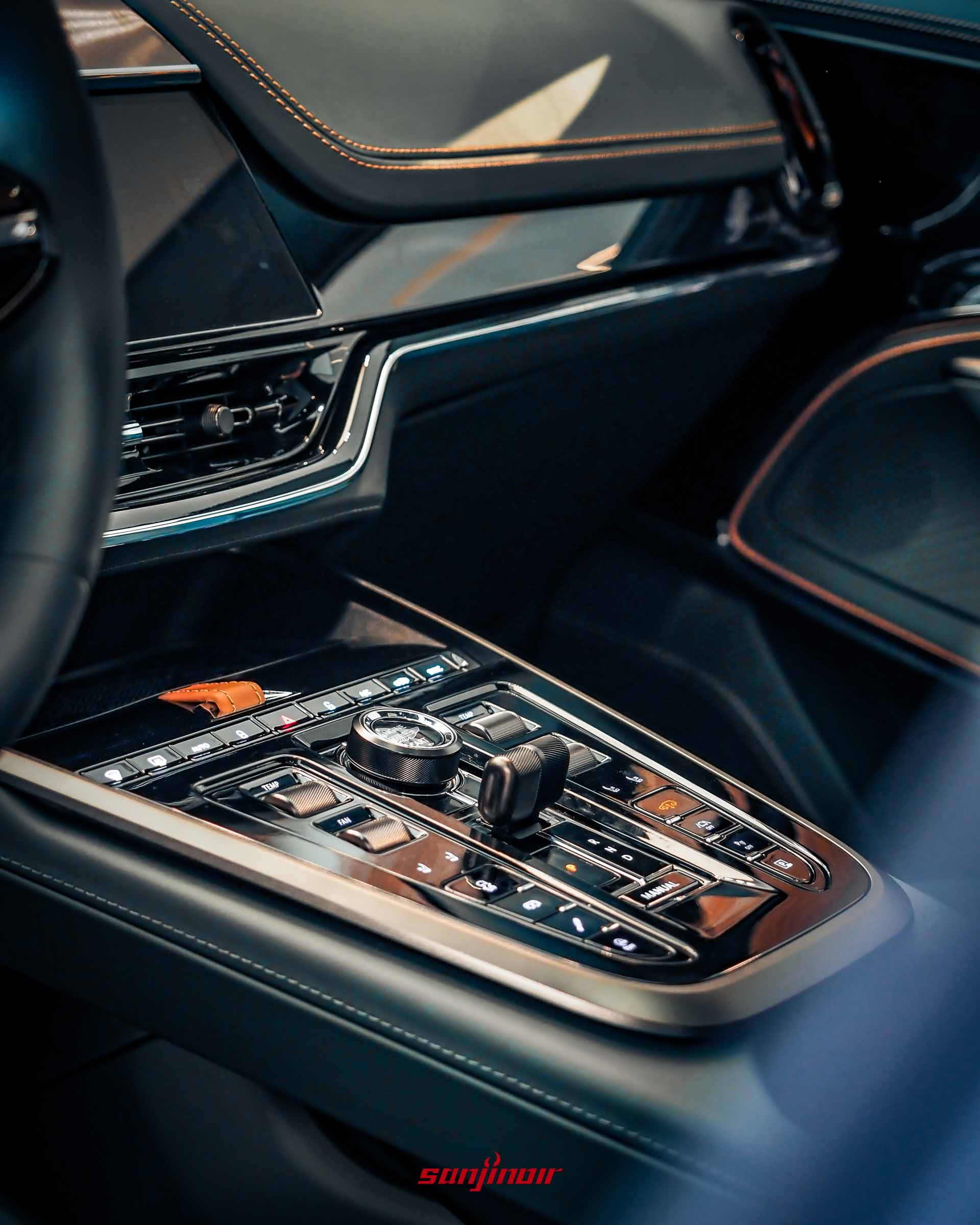 Aston Martin DBX S懸浮式中控台特寫，展示精緻的金屬實體空調按鍵、玻璃觸感旋鈕、排檔按鍵，以及周圍邊框的雙縫線皮革包覆細節。