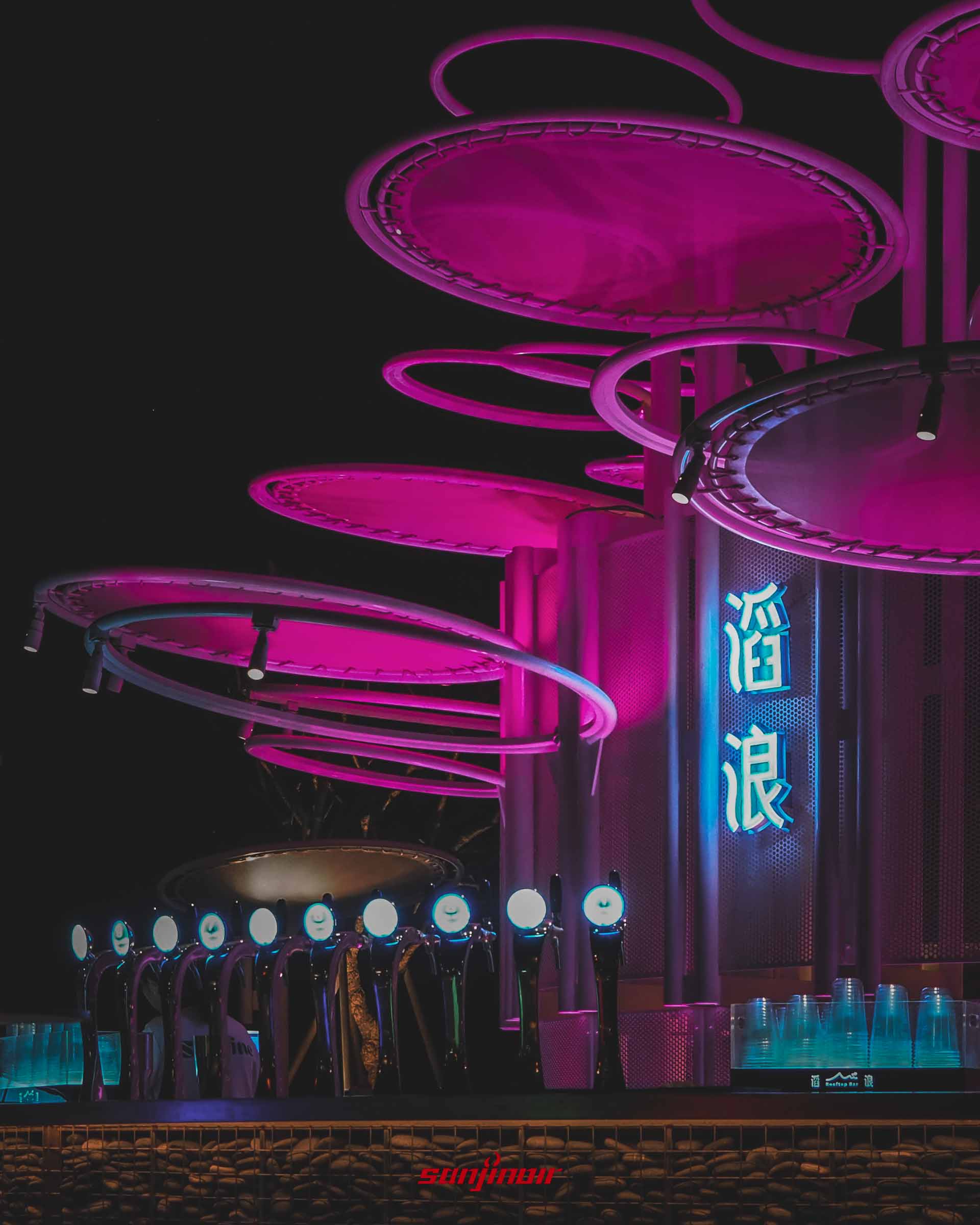 滔浪酒吧的生啤酒機台,一字排開的把手發著光,背景有粉紅色燈光照亮的圓環造型遮棚與滔浪字樣。