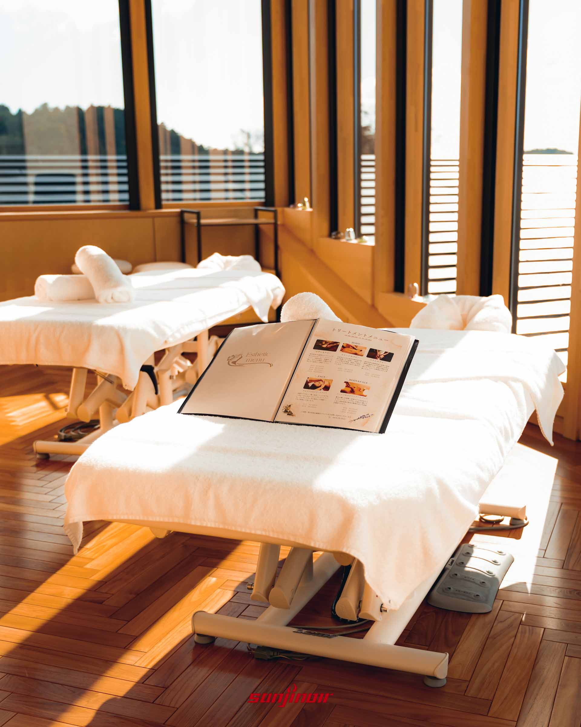 木地板房間內並排著兩張鋪著純白毛巾的 SPA 按摩床，床上翻開著療程目錄，陽光自大面積窗戶透入。