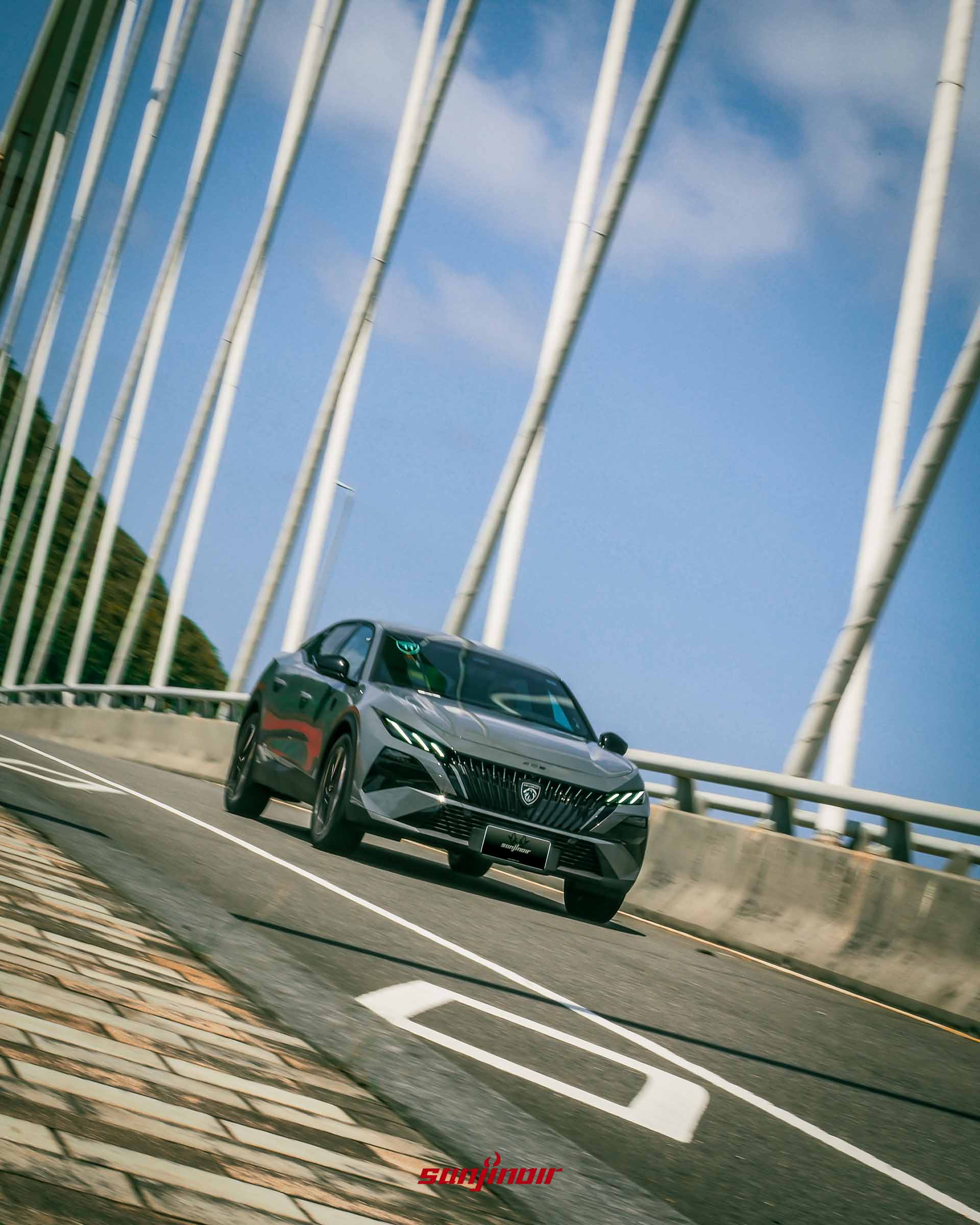 灰色PEUGEOT 408行駛在具有白色鋼纜的橋樑上的車頭動態照片。
