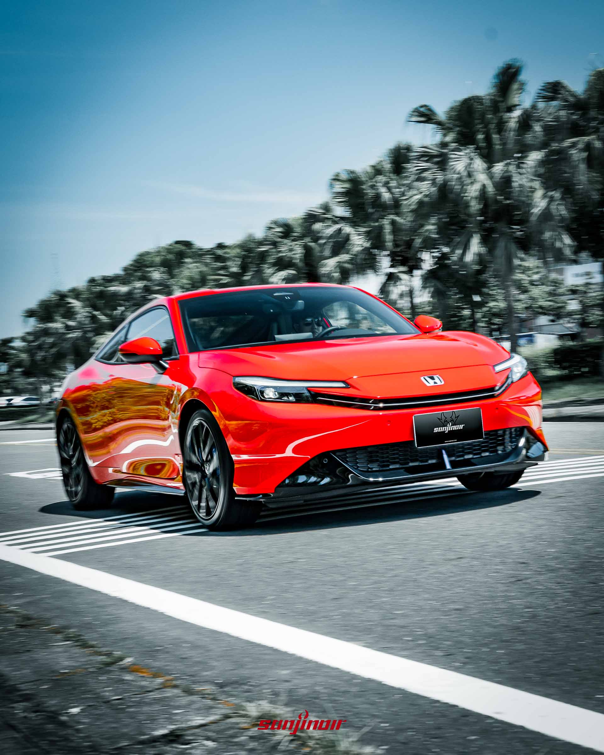 動態追焦攝影,紅色的HONDA Prelude正在道路上行駛,車頭轉向過彎,背景樹木呈現速度感的模糊。