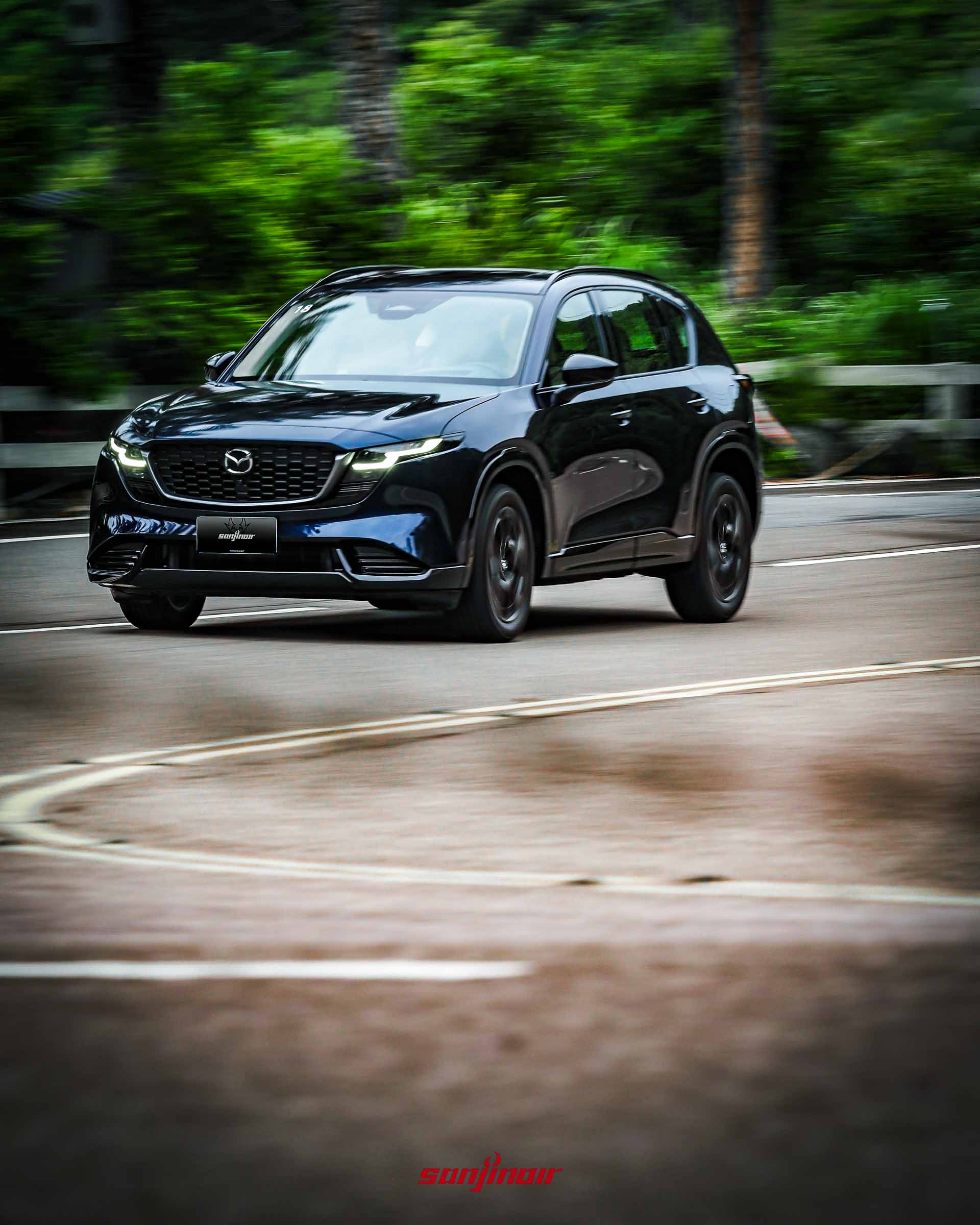 深藍色MAZDA CX-5在山區彎道中高速行駛的車頭側前方動態追焦照。