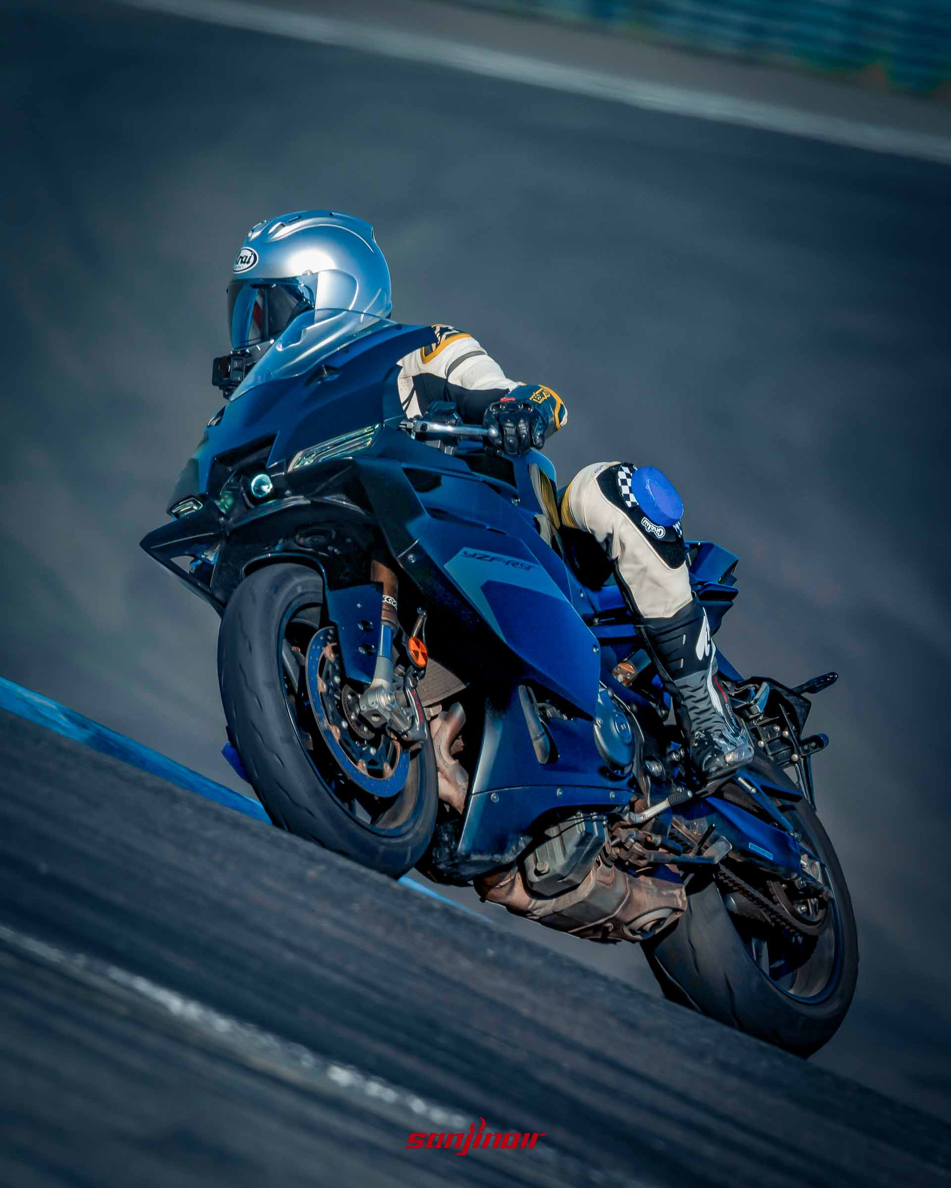 一名穿著淺色防摔衣的騎士駕駛藍色Yamaha YZF-R9在賽道上高速向右側過彎,車體大幅傾倒。