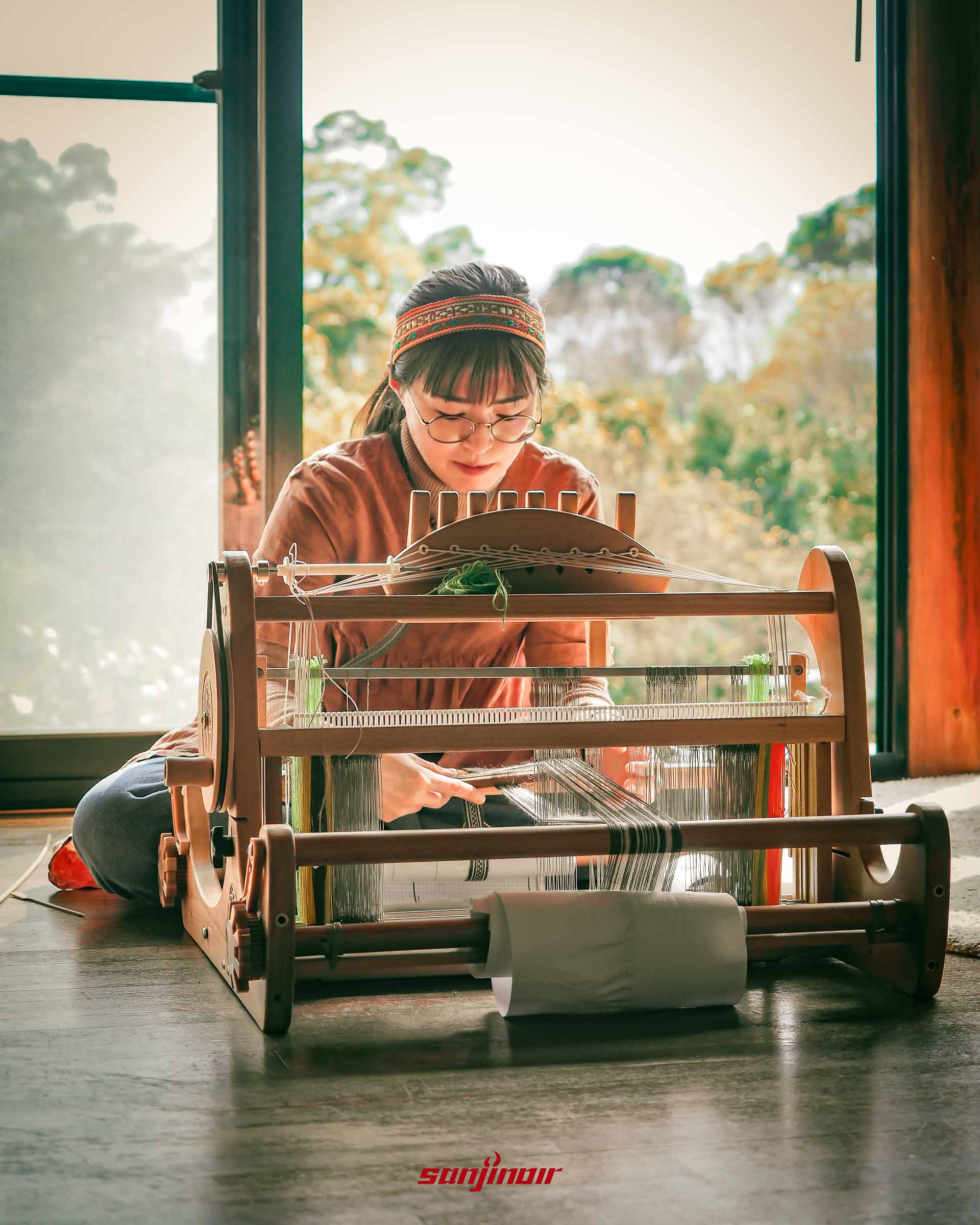 戴著頭飾泰雅族女子坐在地上使用傳統織布機織布。