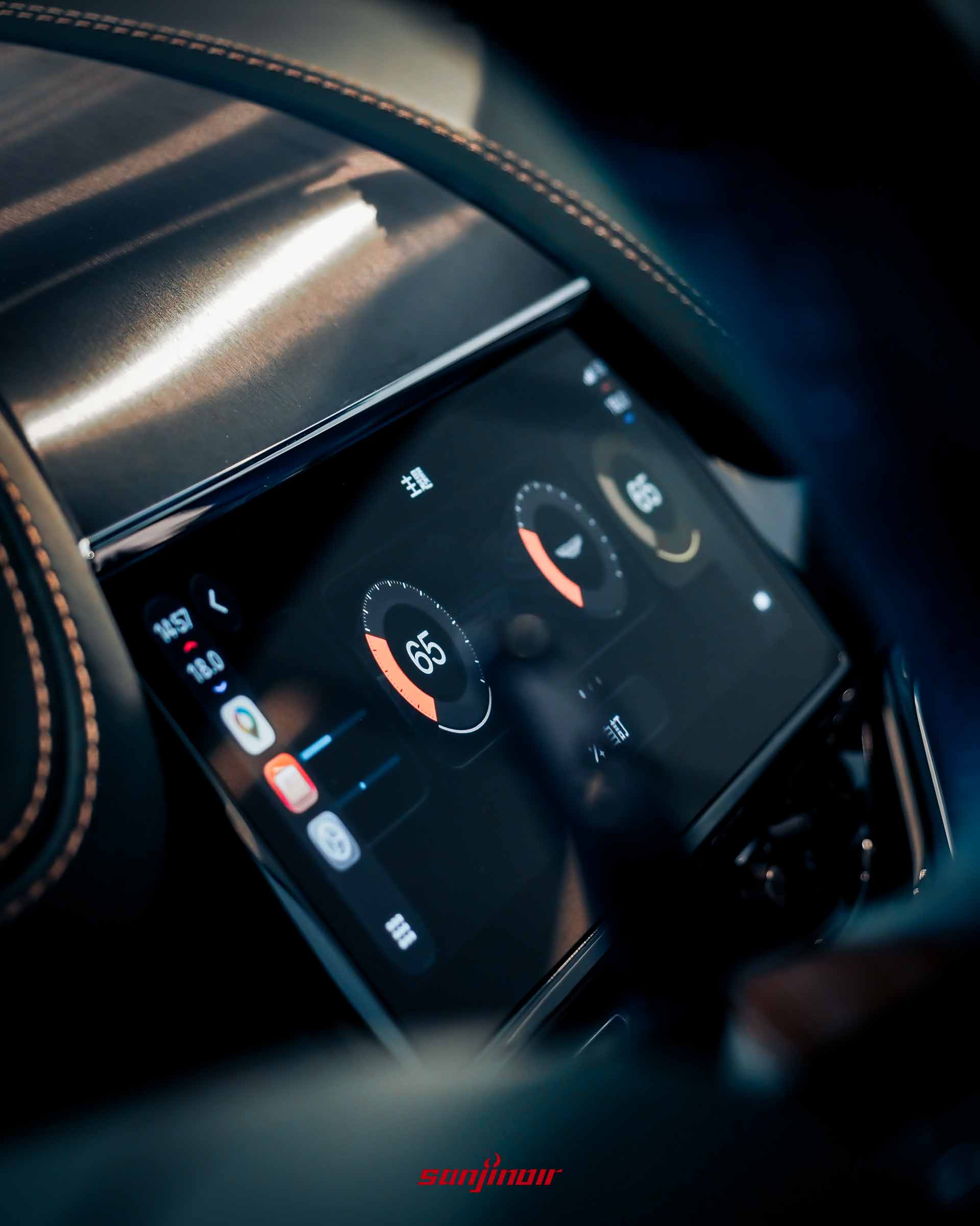 Aston Martin DBX S中控觸控螢幕特寫，螢幕畫面左側顯示著Apple CarPlay的應用程式圖示與導航資訊，右側則為車輛內建的環形數位空調溫度顯示介面。