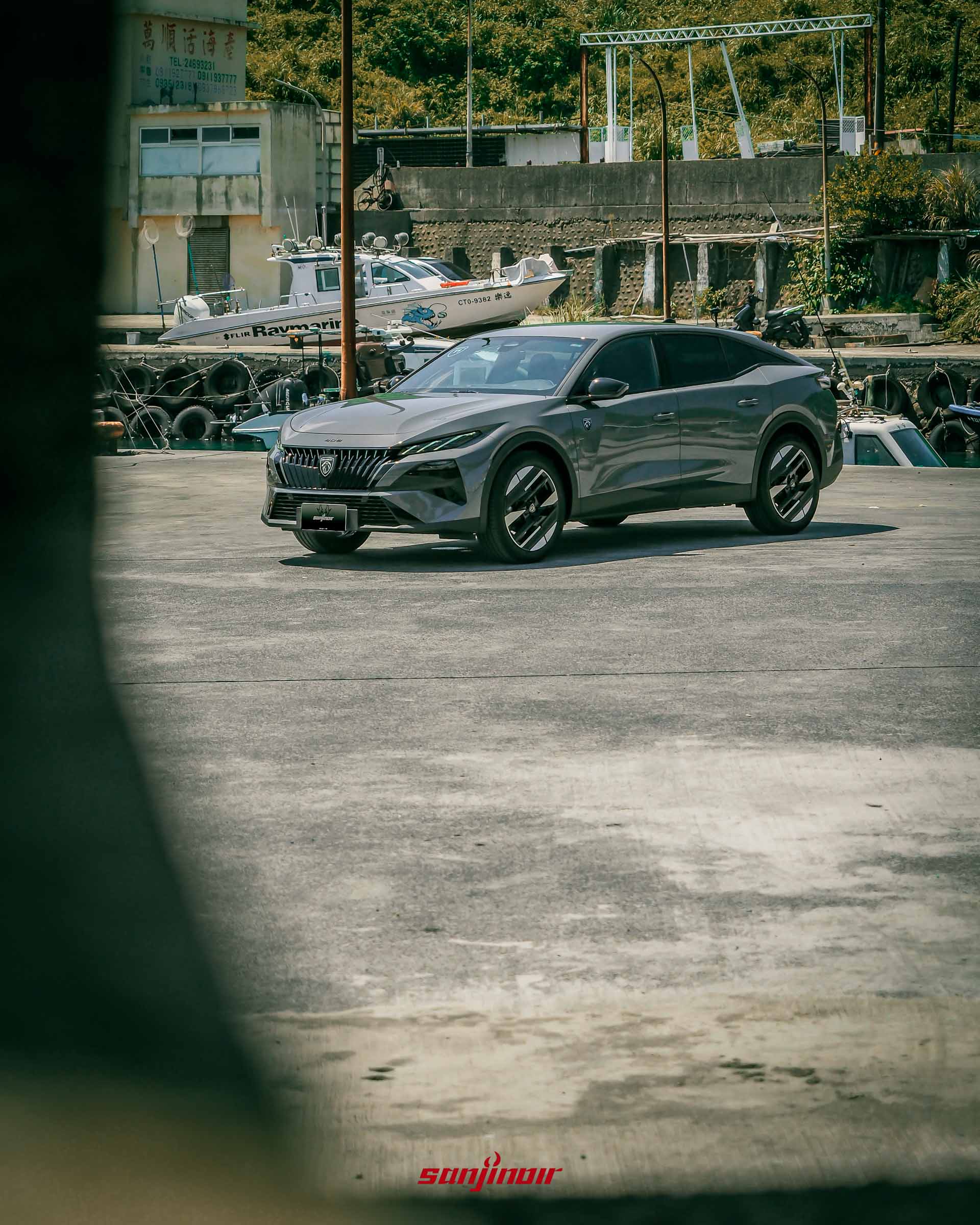 灰色PEUGEOT 408停放在漁港空地的全景,背景有漁船與舊式建築物。