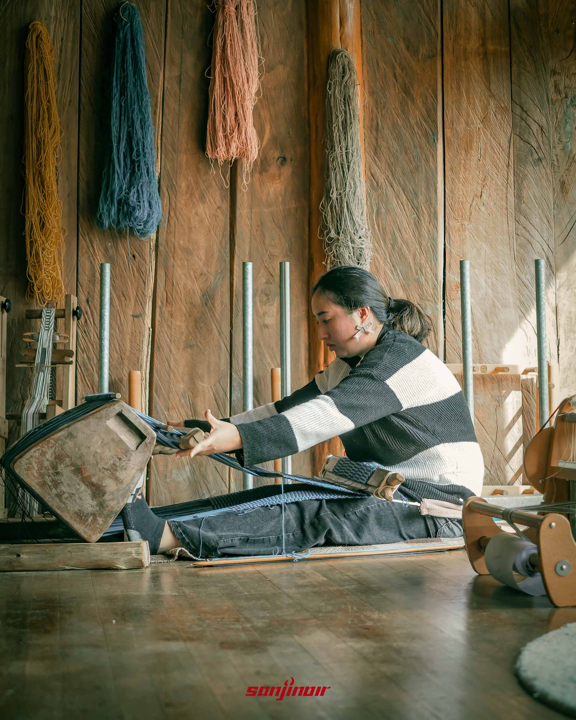 泰雅族女子操作傳統織布機側面照背景牆上掛著彩色紗線。
