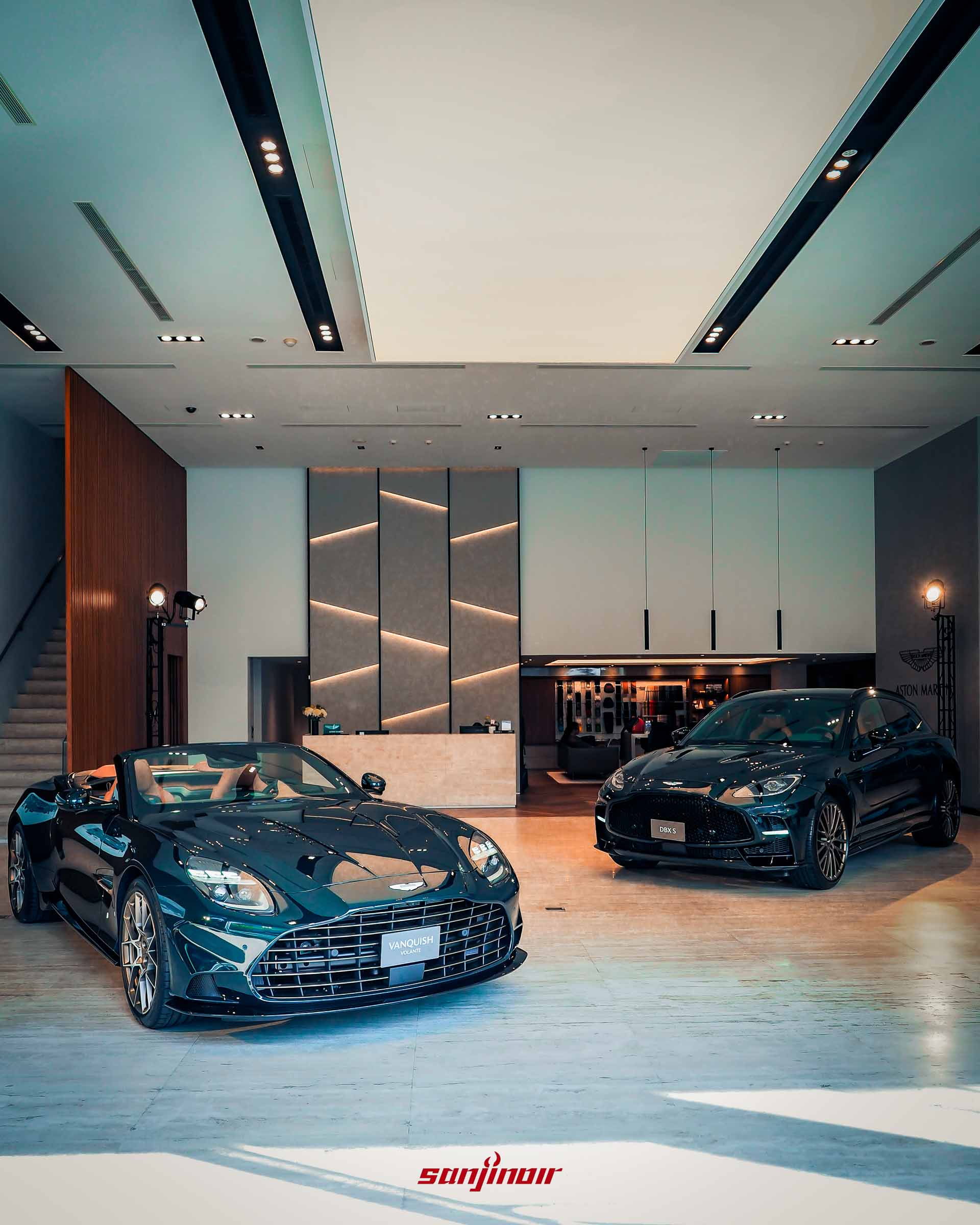 Aston Martin發表會展區全景，左側停放深綠色敞篷開啟狀態的Vanquish Volante 60th Anniversary Edition，右側停放同為深綠色漆面的DBX S高性能休旅車，展場佈置呈現高雅奢華的現代風格。