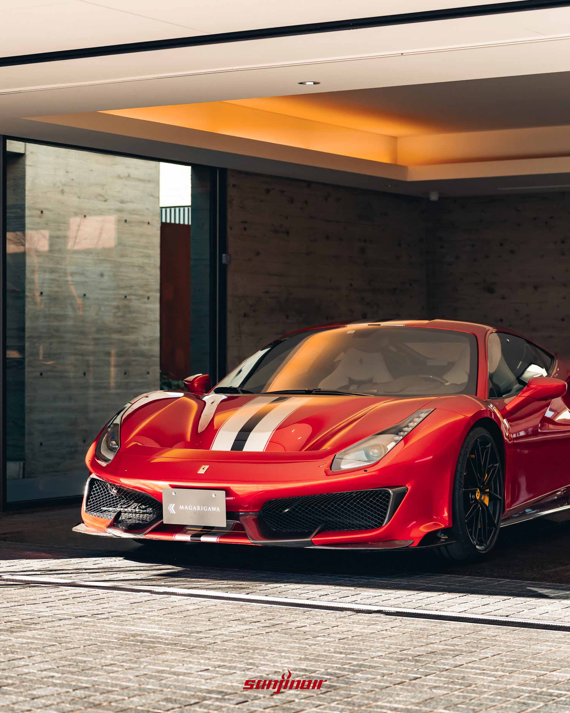 一輛紅色 Ferrari 跑車停放於水泥質感的半開放式室內車庫中，車身反射著戶外的自然光線。