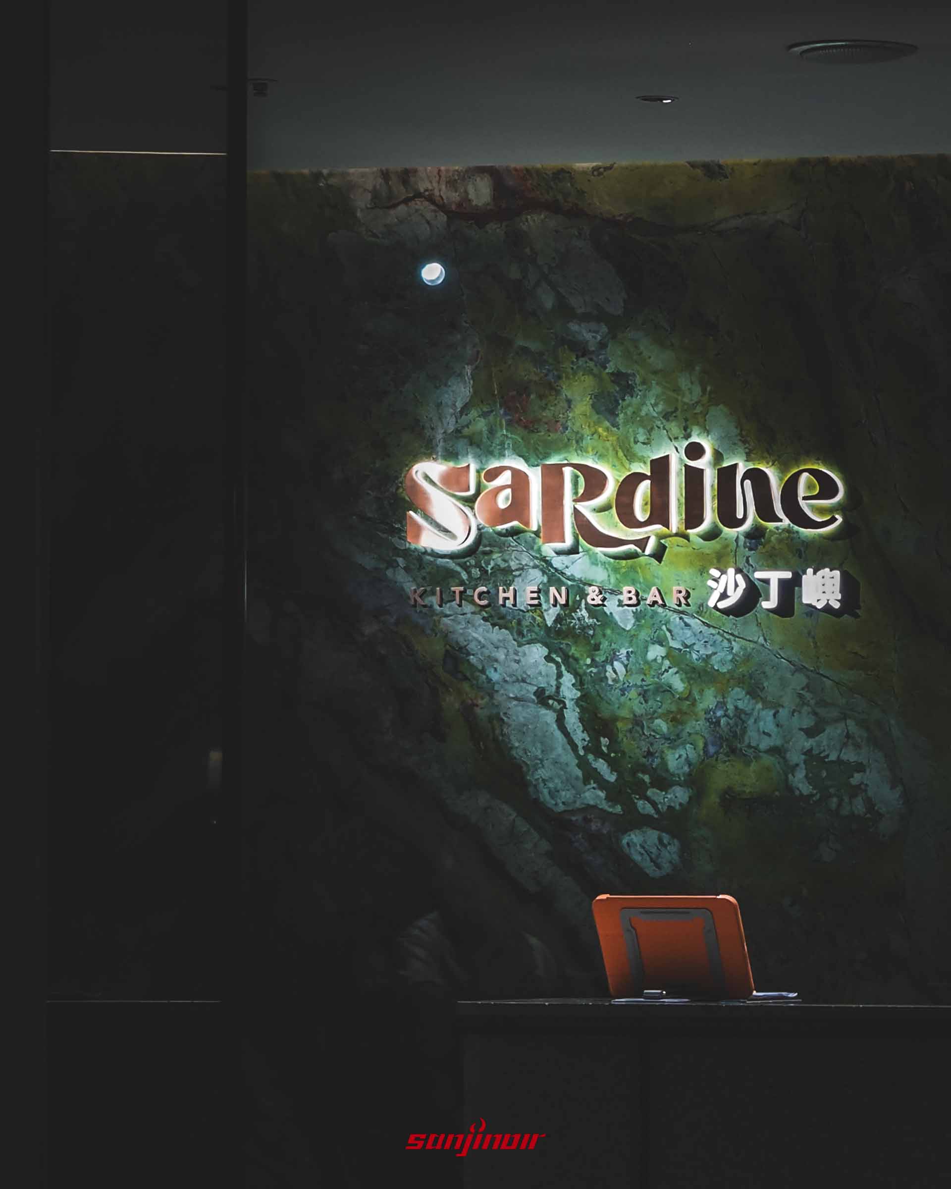 餐廳入口櫃檯,綠色大理石紋理的牆面上掛著發光的Sardine KITCHEN&BAR沙丁嶼字樣。