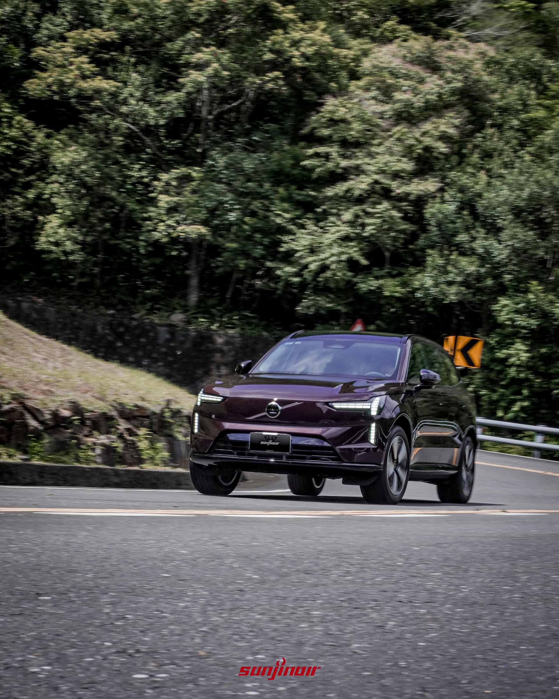 Volvo EX90在山路中行駛的正前側動態照,車輛正駛出彎道,展現穩定的車身動態。
