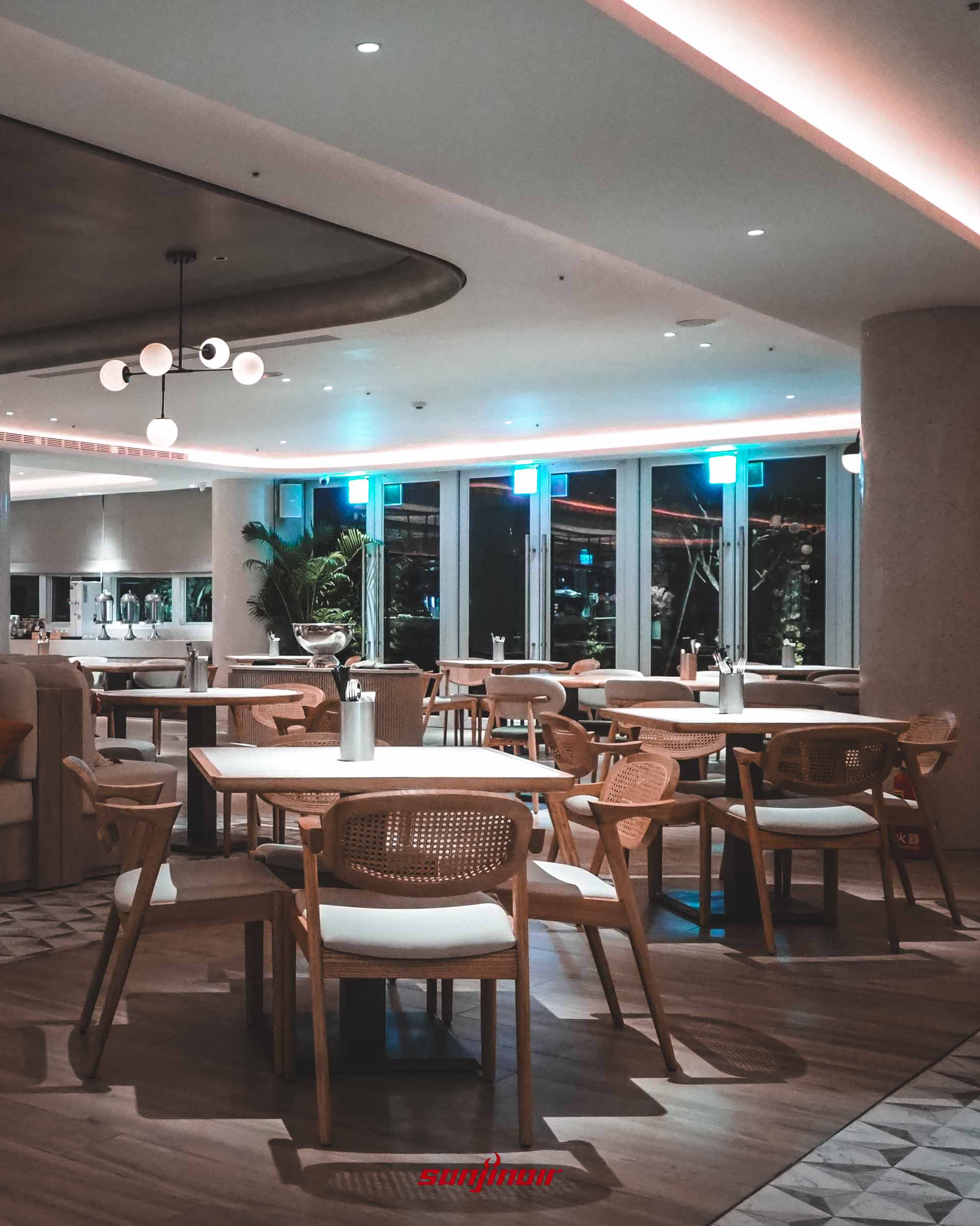 沙丁嶼餐廳內部,溫暖燈光下擺放著多張木質與藤編座椅搭配白桌面,大面落地窗外是夜晚景色。
