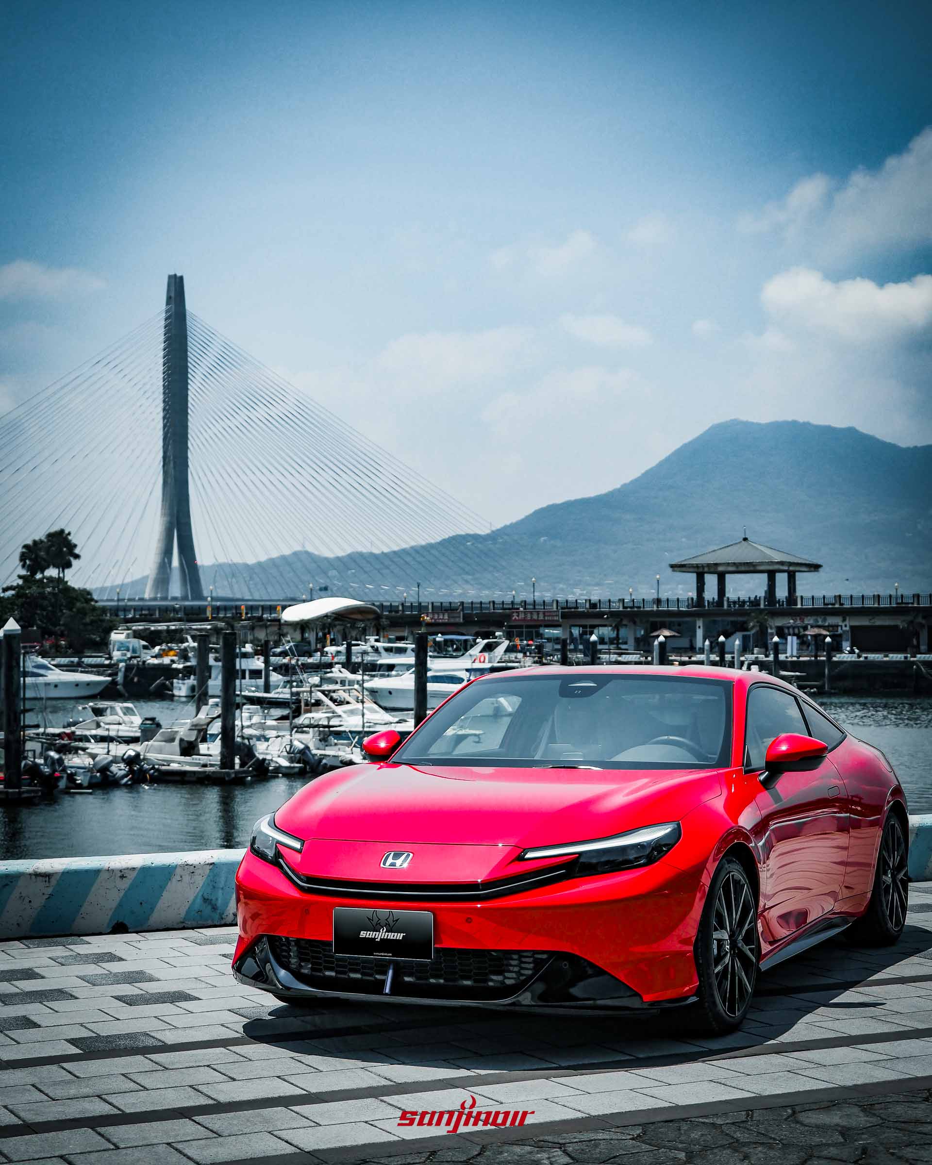 靜態拍攝紅色的HONDA Prelude停放於港灣廣場,車頭面向鏡頭,後方矗立著淡江大橋與遠山。