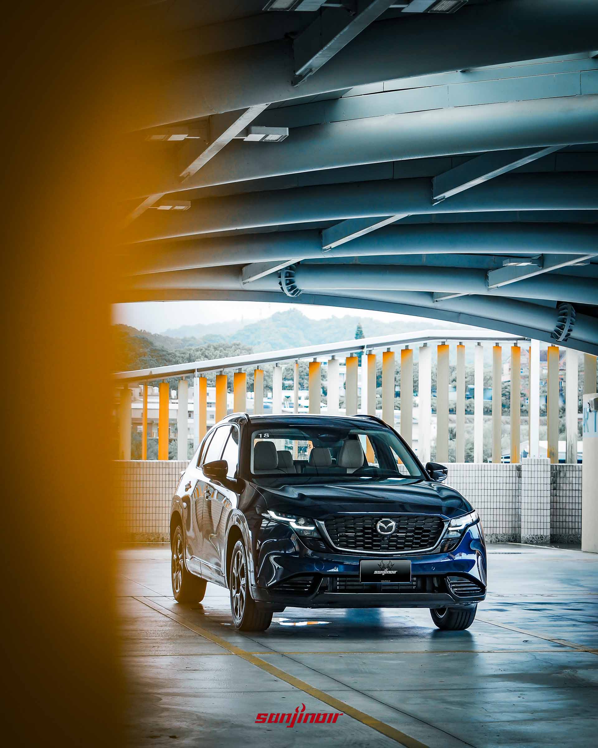 MAZDA CX-5停放於停車場的正前方遠景照,透過黃色柱子作為前景框架。