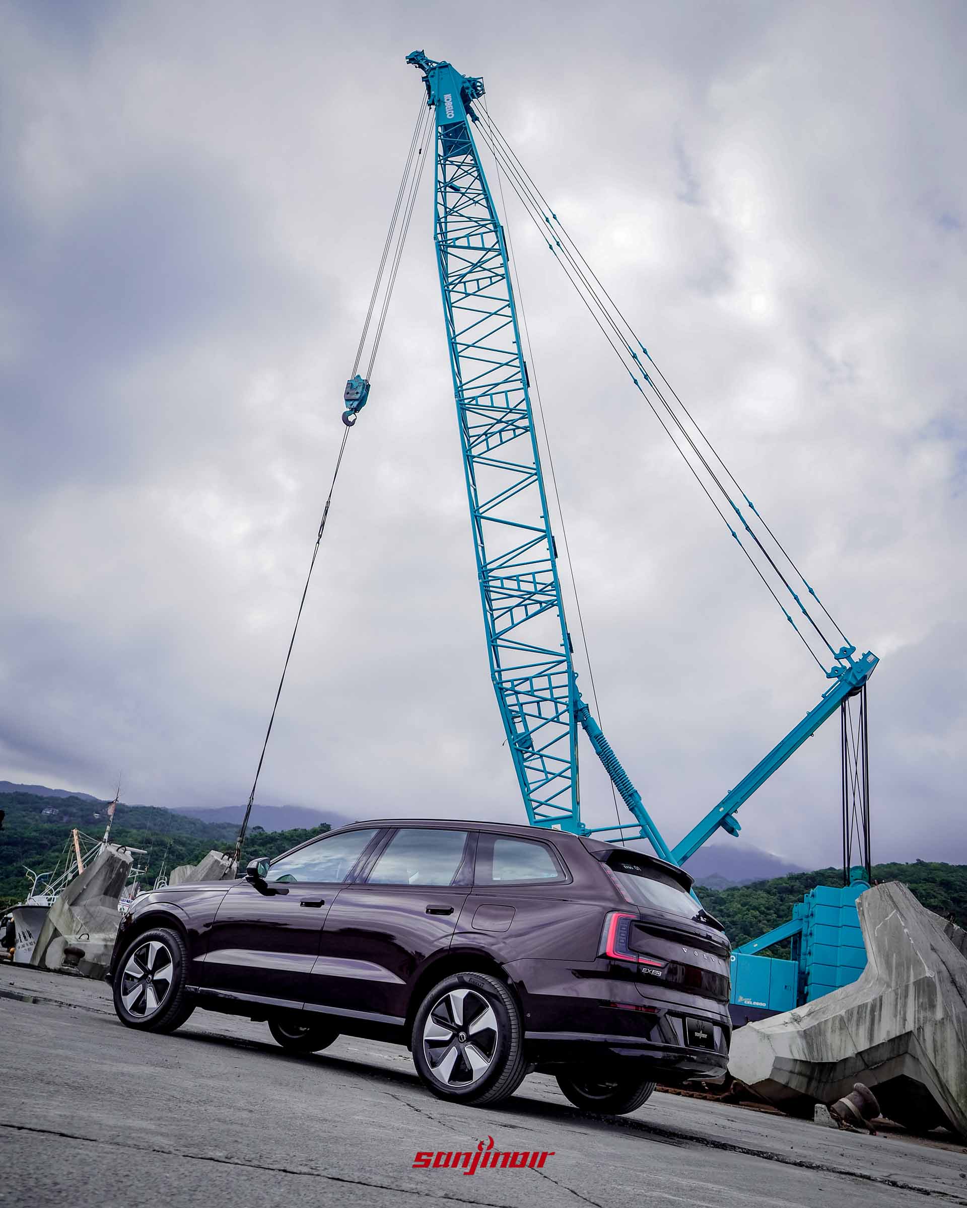 野莓紅Volvo EX90停放在港口,後方矗立著一座巨大的淺藍色工程吊車,形成強烈的視覺對比。
