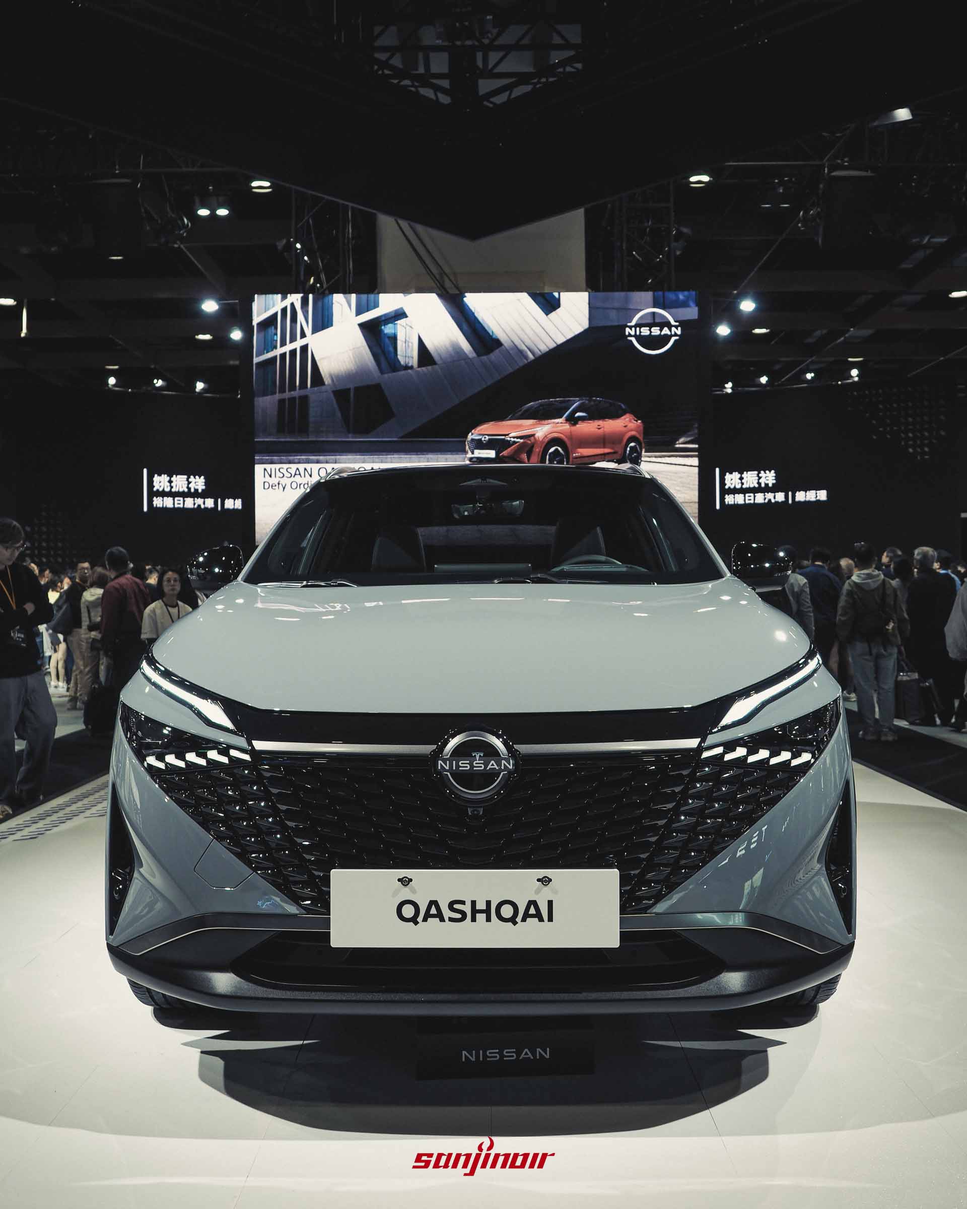 灰色Nissan Qashqai e-POWER休旅車正面特寫，背景螢幕顯示Nissan品牌標誌。