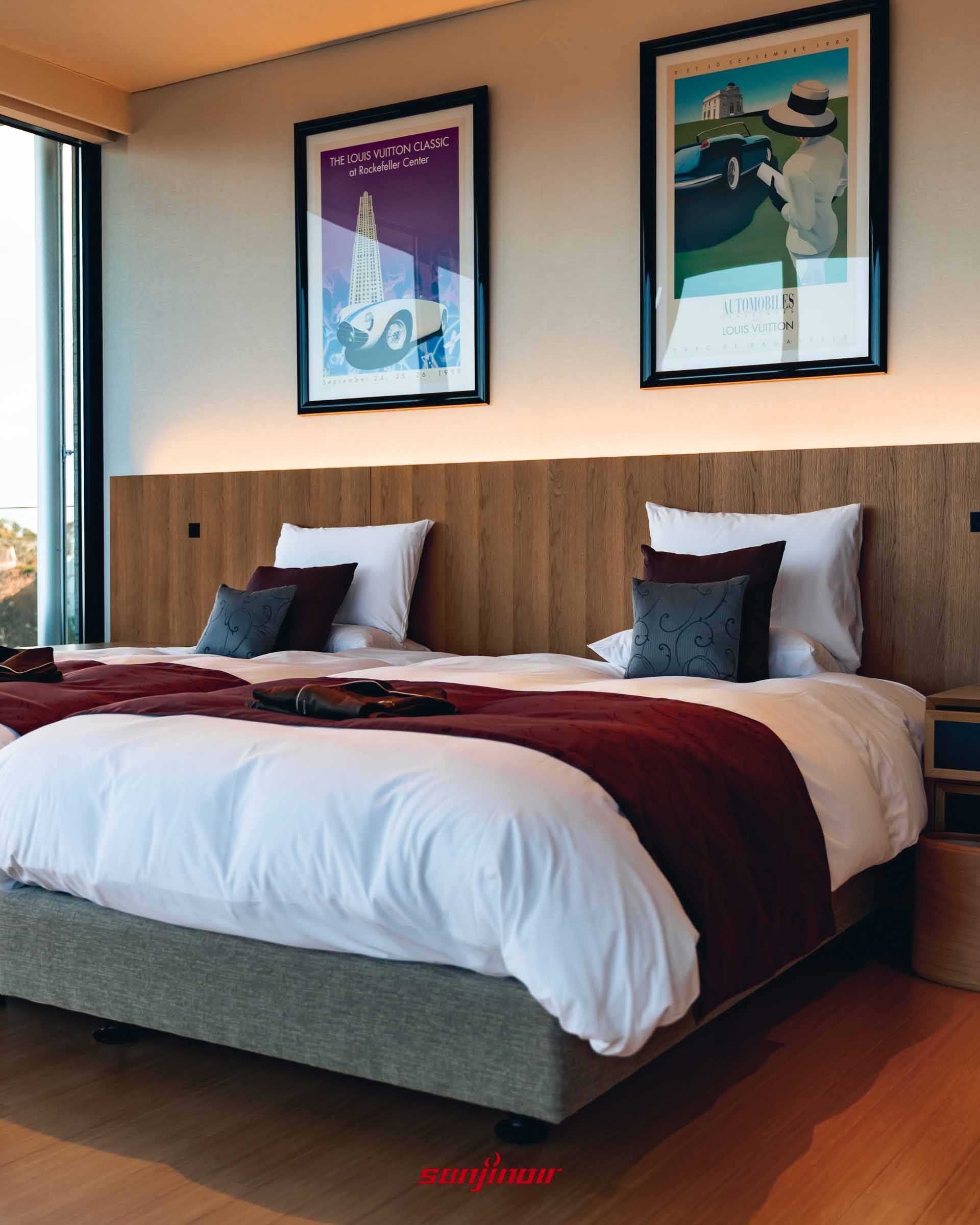 鋪設深紅色床布的雙人床鋪，木質床頭板上方掛有兩幅Louis Vuitton骨董車主題藝術海報，室內透著溫暖的間接照明。