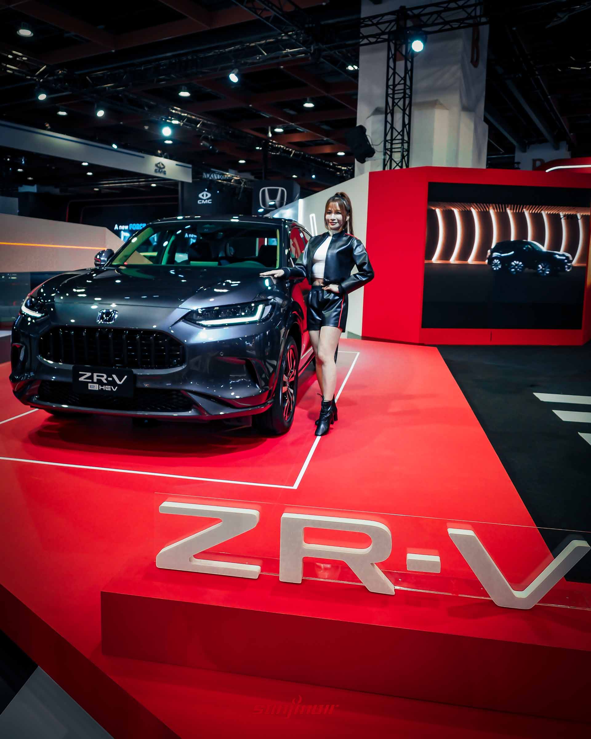 深灰色Honda ZR-V e:HEV休旅車與車模合影，背景為紅色Honda展區背板。