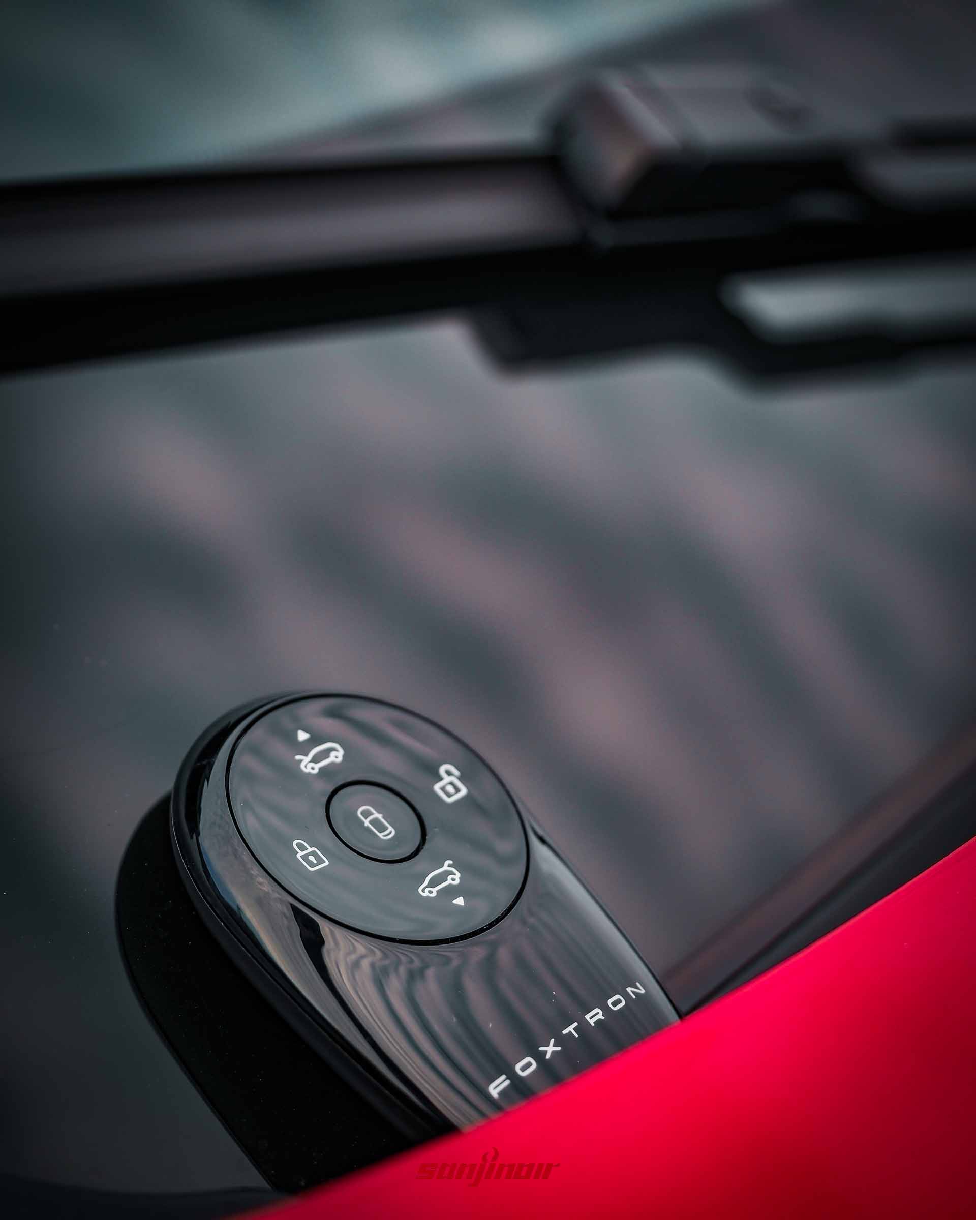 放置在車體上，帶有FOXTRON字樣與車輛圖示的黑色鵝卵石造型智能鑰匙特寫。