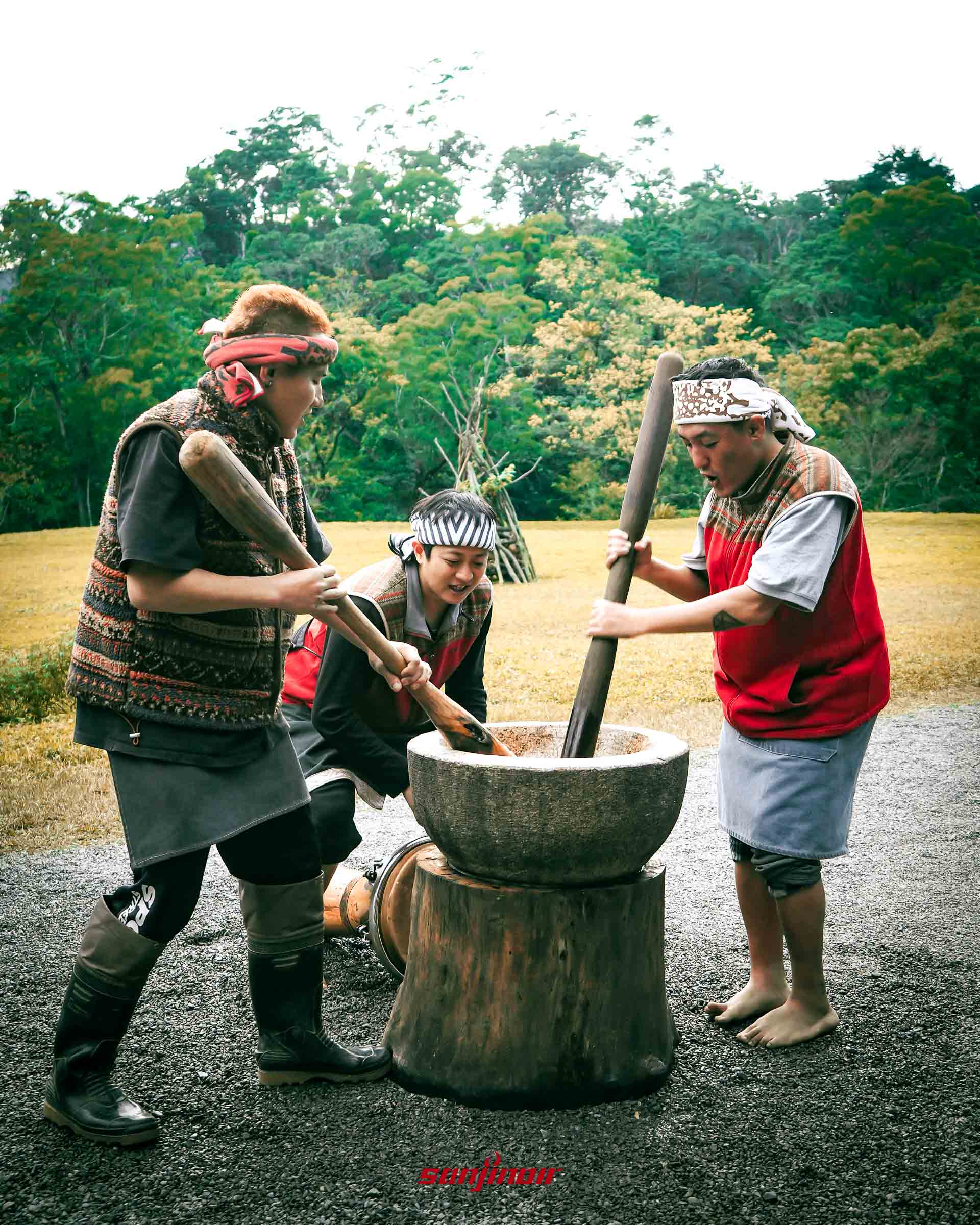 三人合力使用木杵在巨大木臼中搗麻糬。