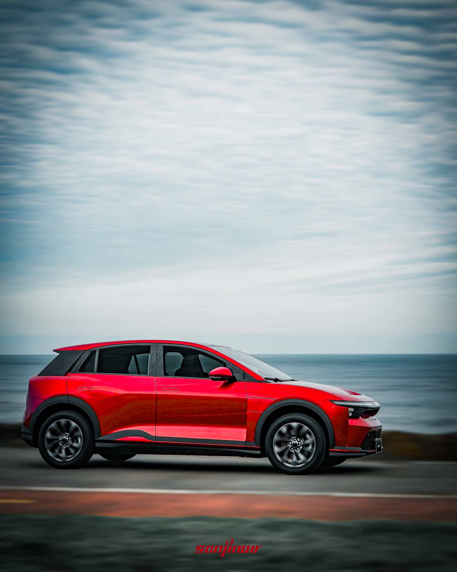 紅色Foxtron Bria Emerge在海岸公路上行駛的正側面動態追焦照片。